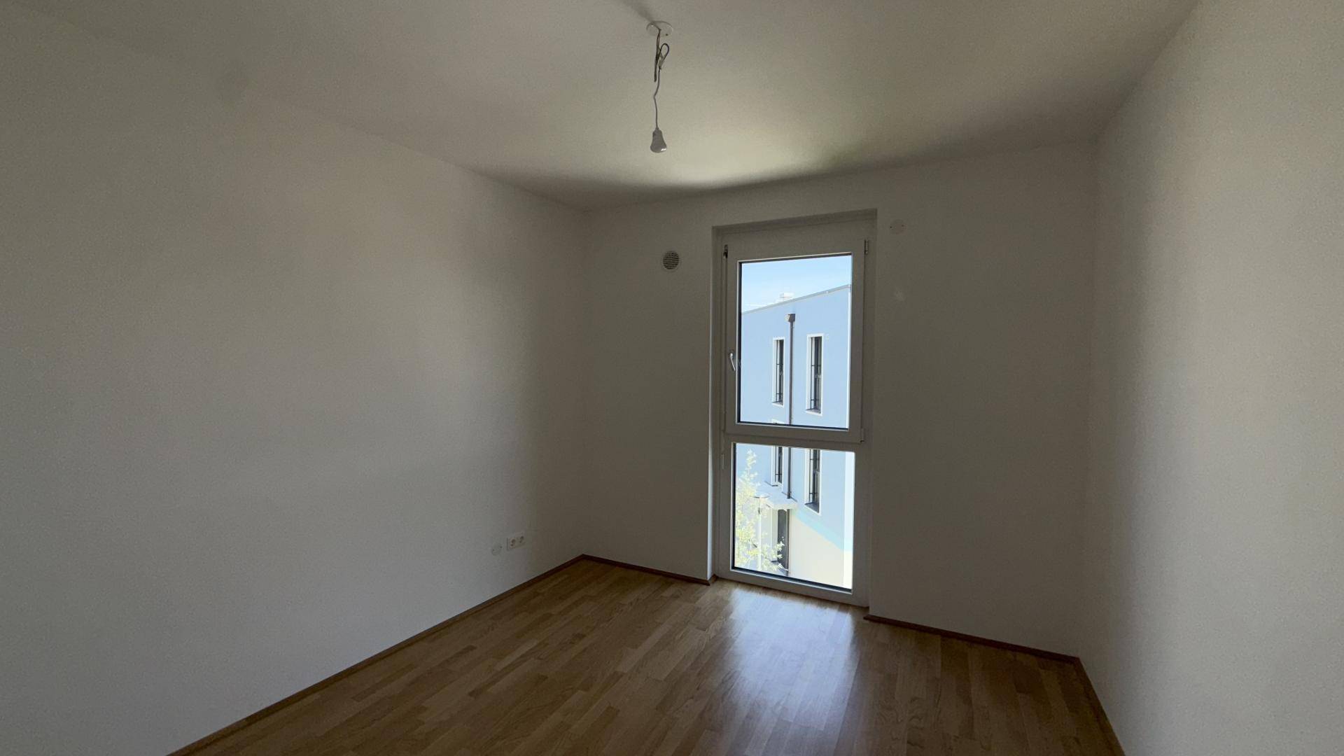 Helles Schlafzimmer mit Holzparkett und Blick auf die moderne Architektur des angrenzenden Gebäudes.