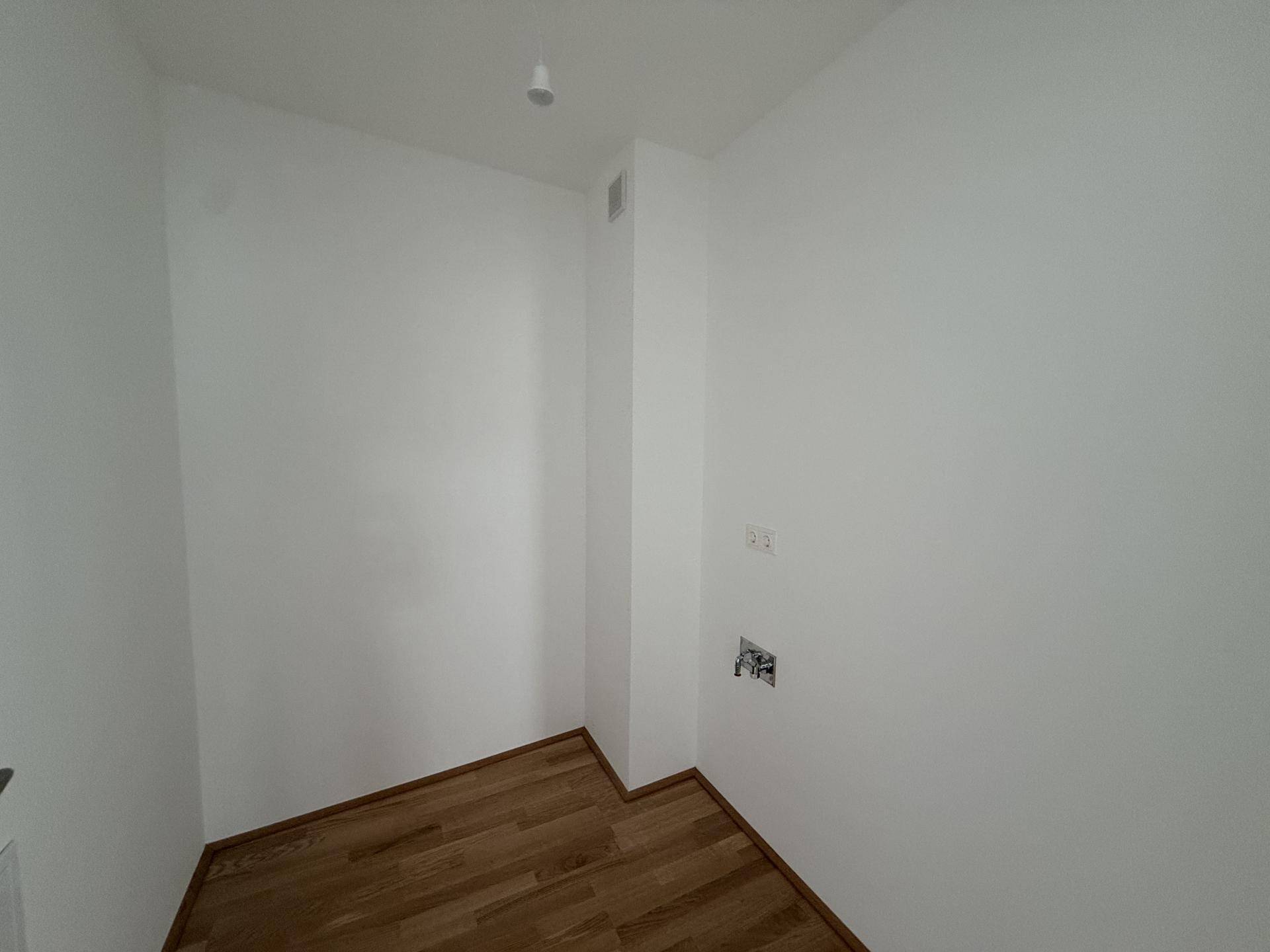 Kleiner, heller Raum mit Holzboden und weißen Wänden, ideal als Abstellraum nutzbar.