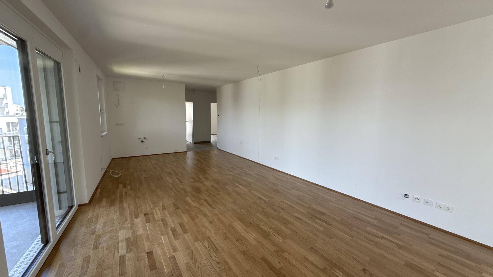 Geräumiges Wohnzimmer mit Holzboden, großen Fenstern und Blick in den angrenzenden Flur.
