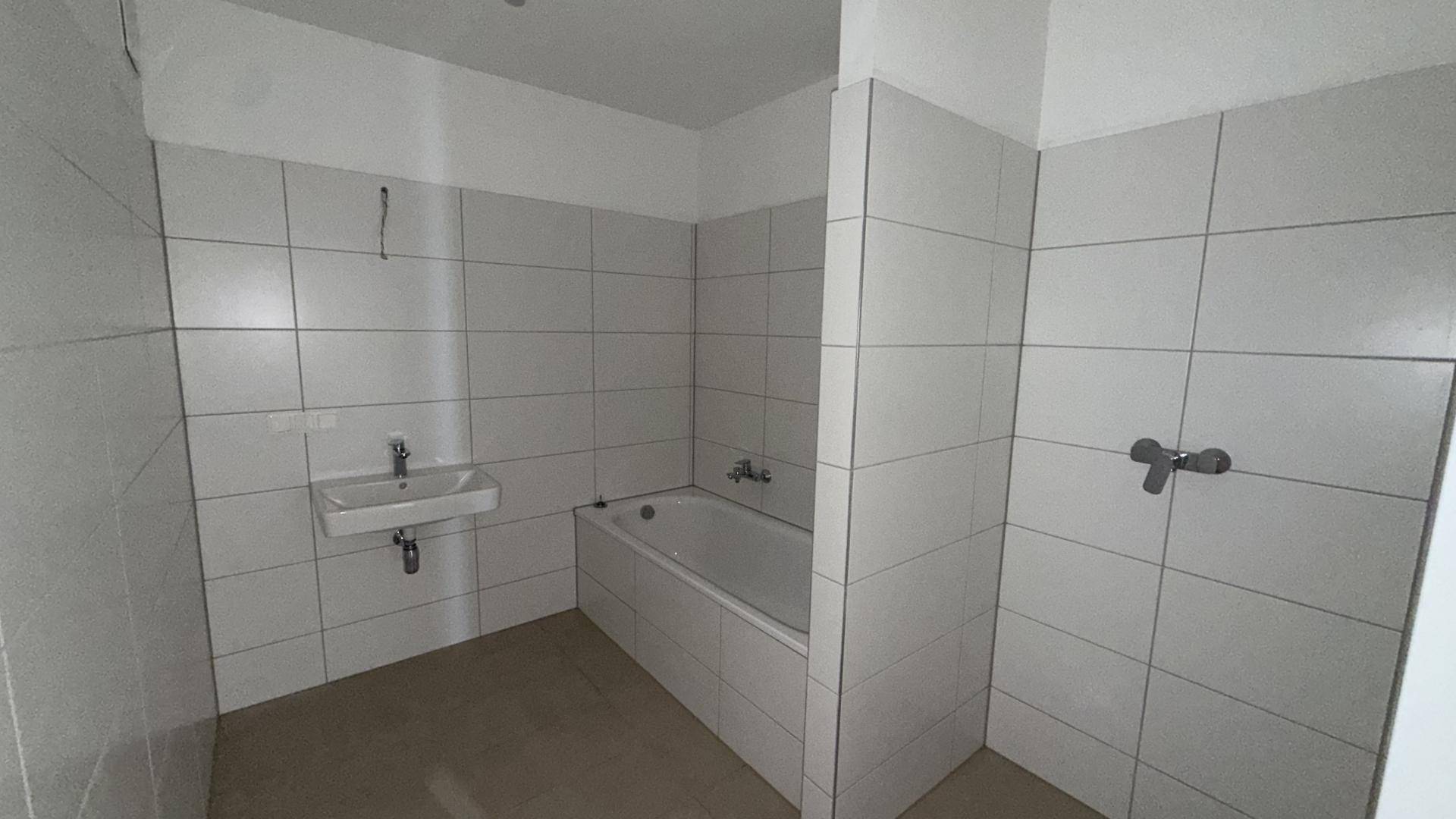 Unfertiges Badezimmer mit weißen Fliesen, Badewanne und Waschbecken, bereit für den Ausbau.