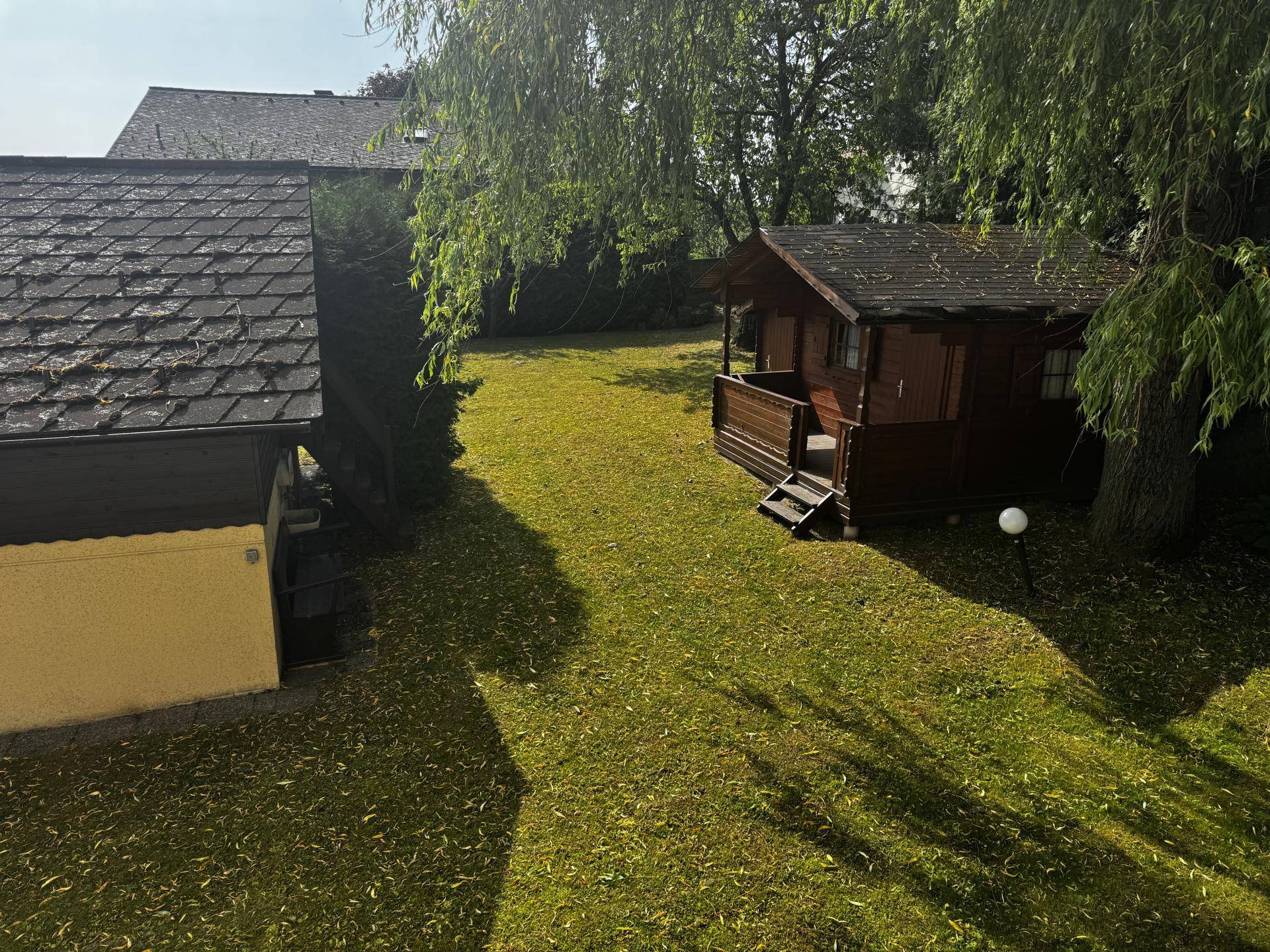 Blick von oben auf den weitläufigen Garten mit Gartenhaus und viel Grünfläche.