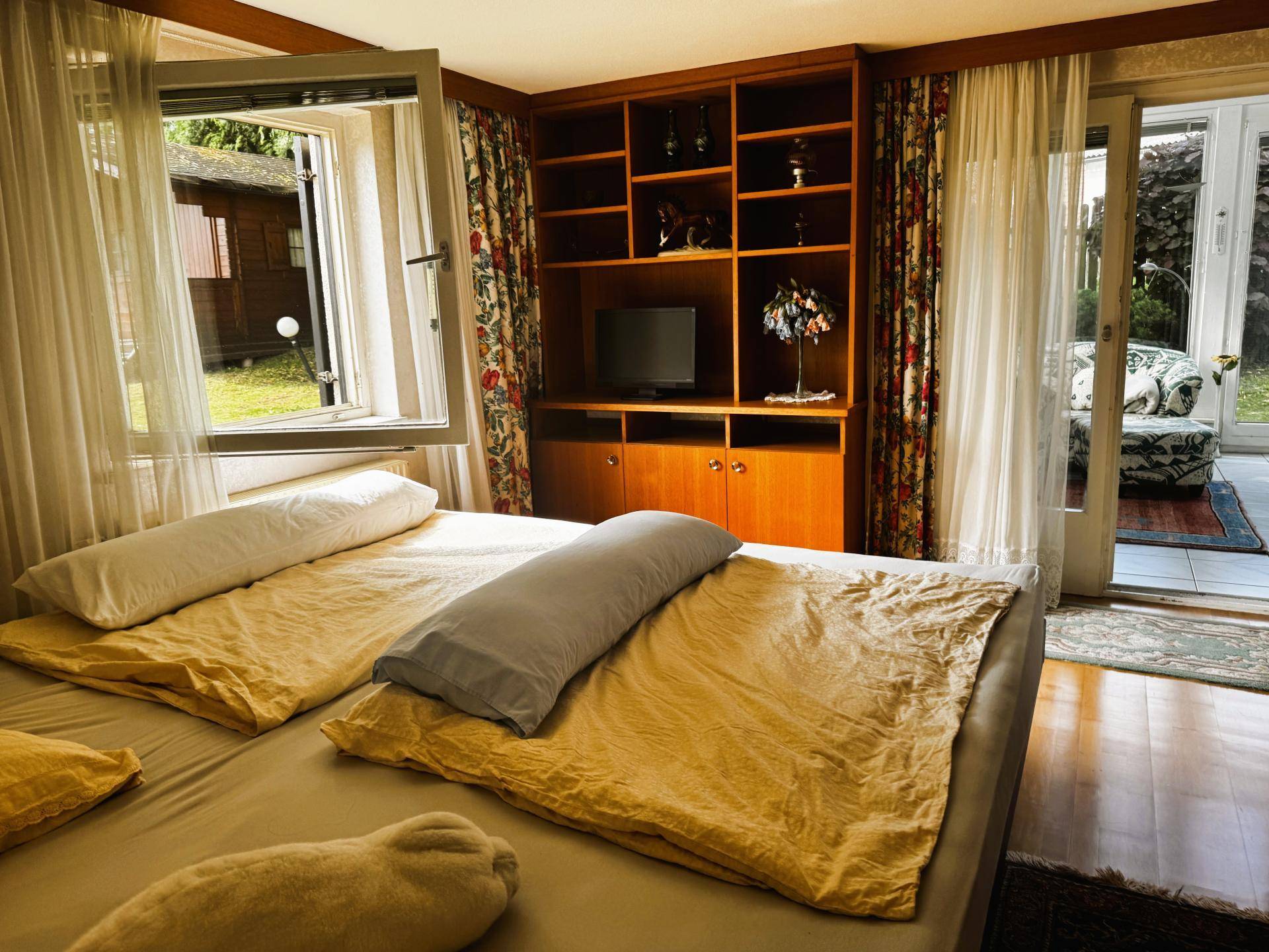 Schlafzimmer mit Doppelbett, Holzregal und direktem Zugang zum sonnigen Wintergarten.