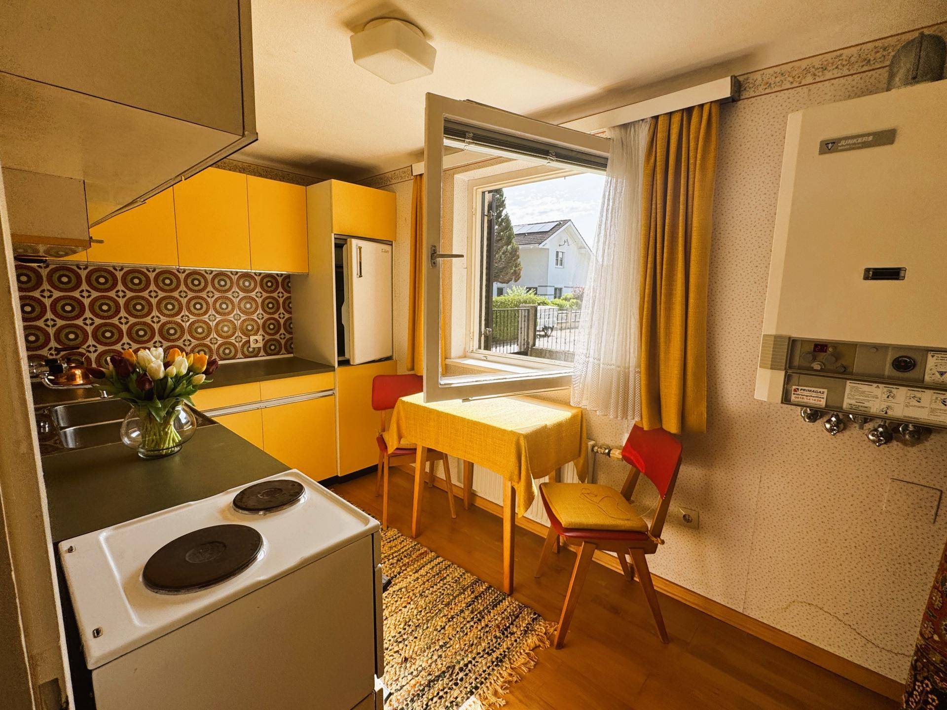 Kleine Küche mit gelben Schränken, Essbereich und Fenster mit Blick nach draußen.