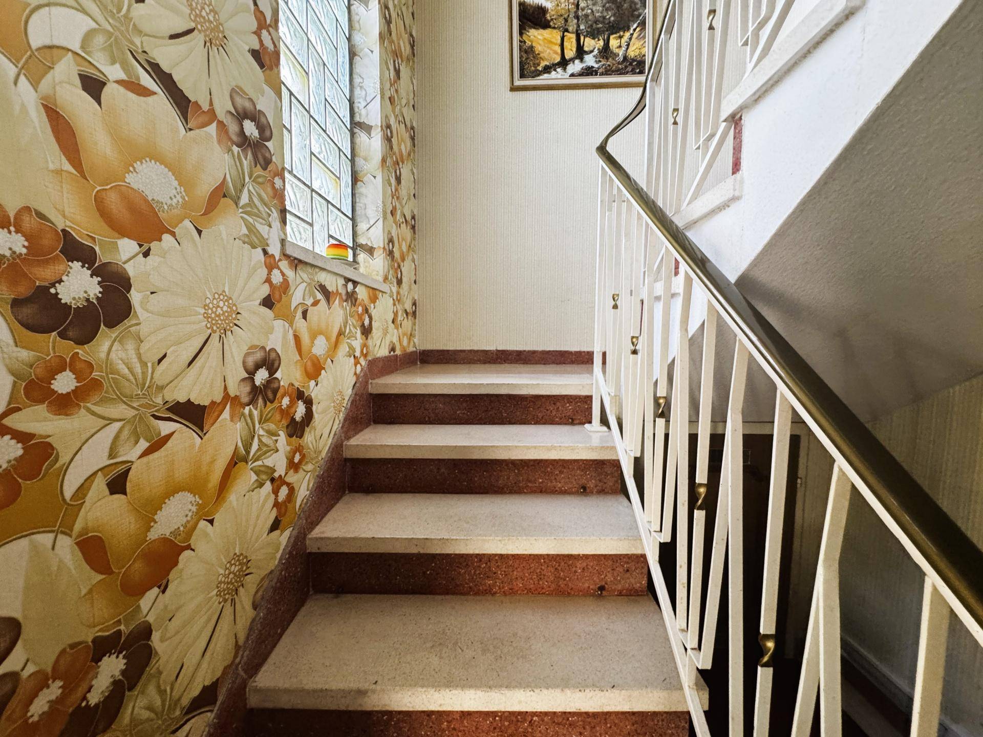 Treppenhaus mit auffälliger Blumentapete und Geländer im Vintage-Stil.