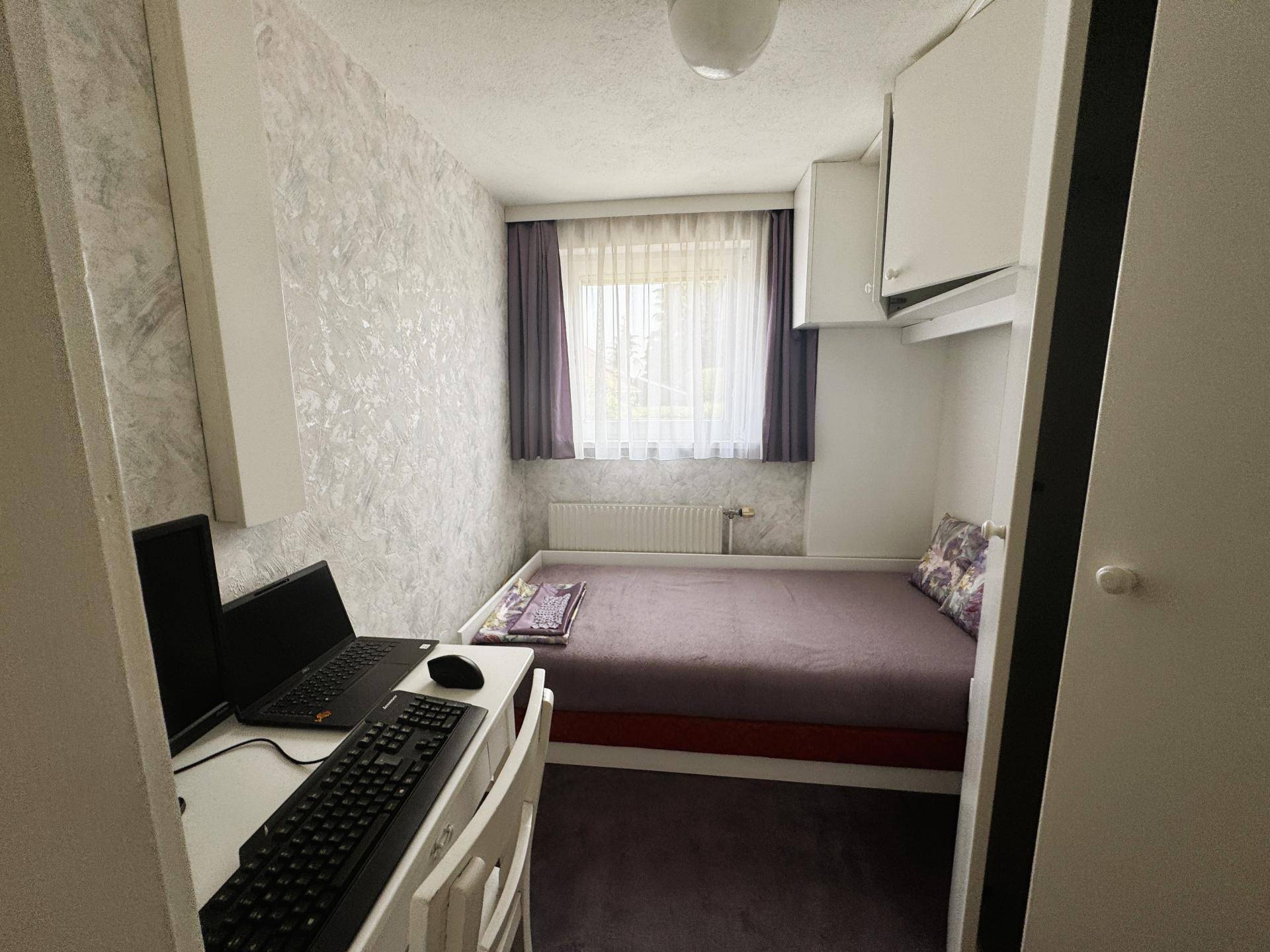 Kleines Schlafzimmer mit Bett, Schreibtisch und Fenster, ideal als Kinder- oder Gästezimmer.