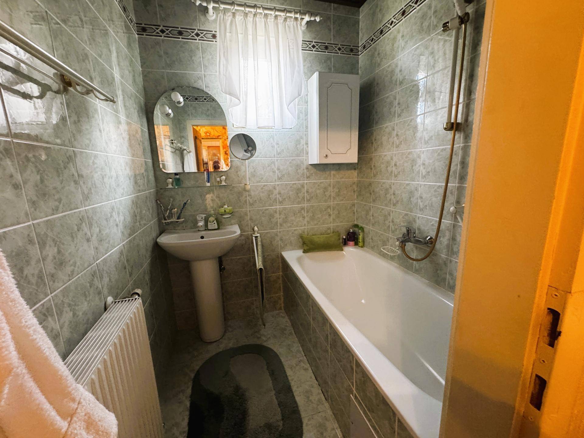Badezimmer mit Badewanne, Waschbecken und grauen Fliesen an Wänden und Boden.