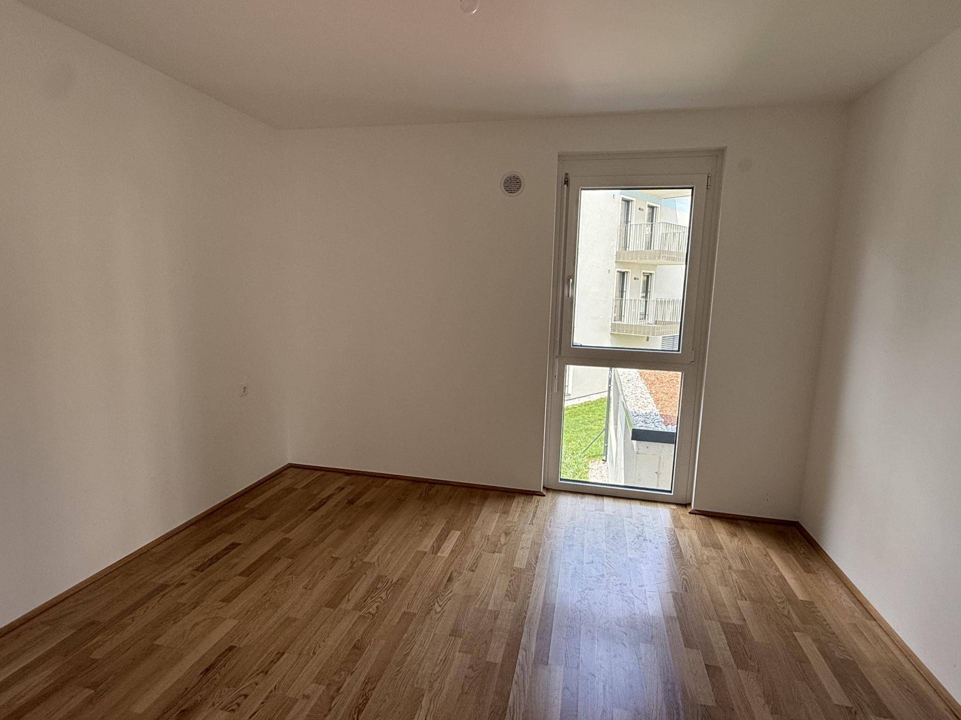 Weiteres Schlafzimmer mit Parkettboden, weißen Wänden und einem großen Fenster mit Blick auf die Umgebung.