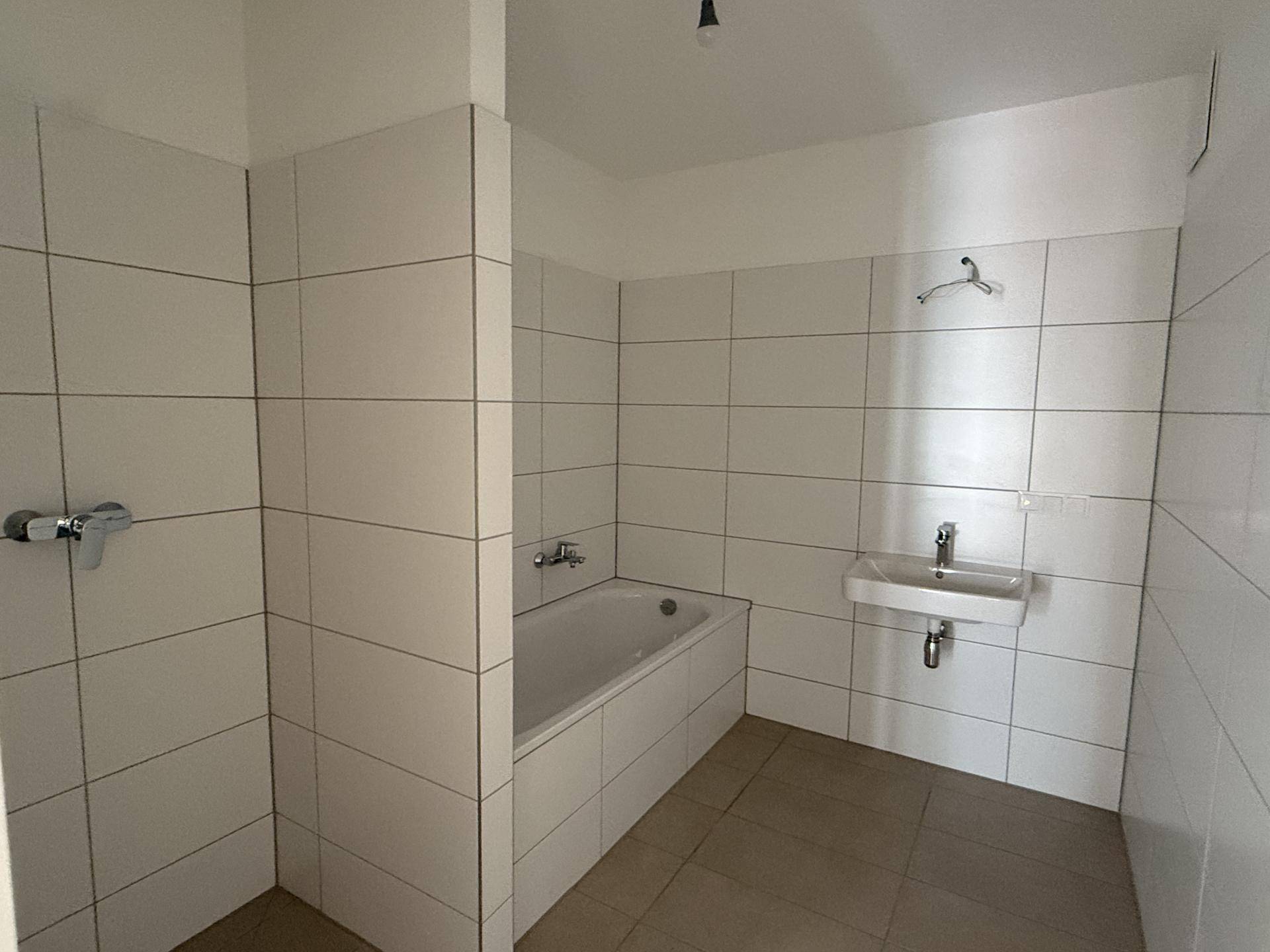 Modernes Badezimmer mit weißen Fliesen, einer Badewanne und einem einzelnen Waschbecken.