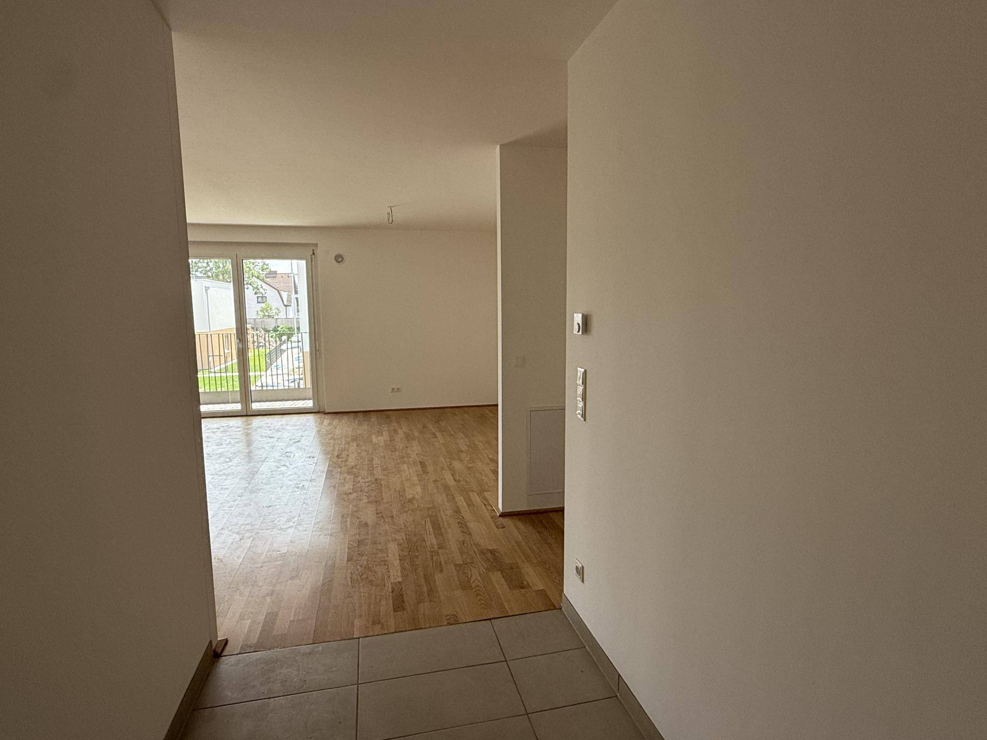Heller Eingangsbereich mit Fliesenboden, der in einen Wohnbereich mit Parkett übergeht.