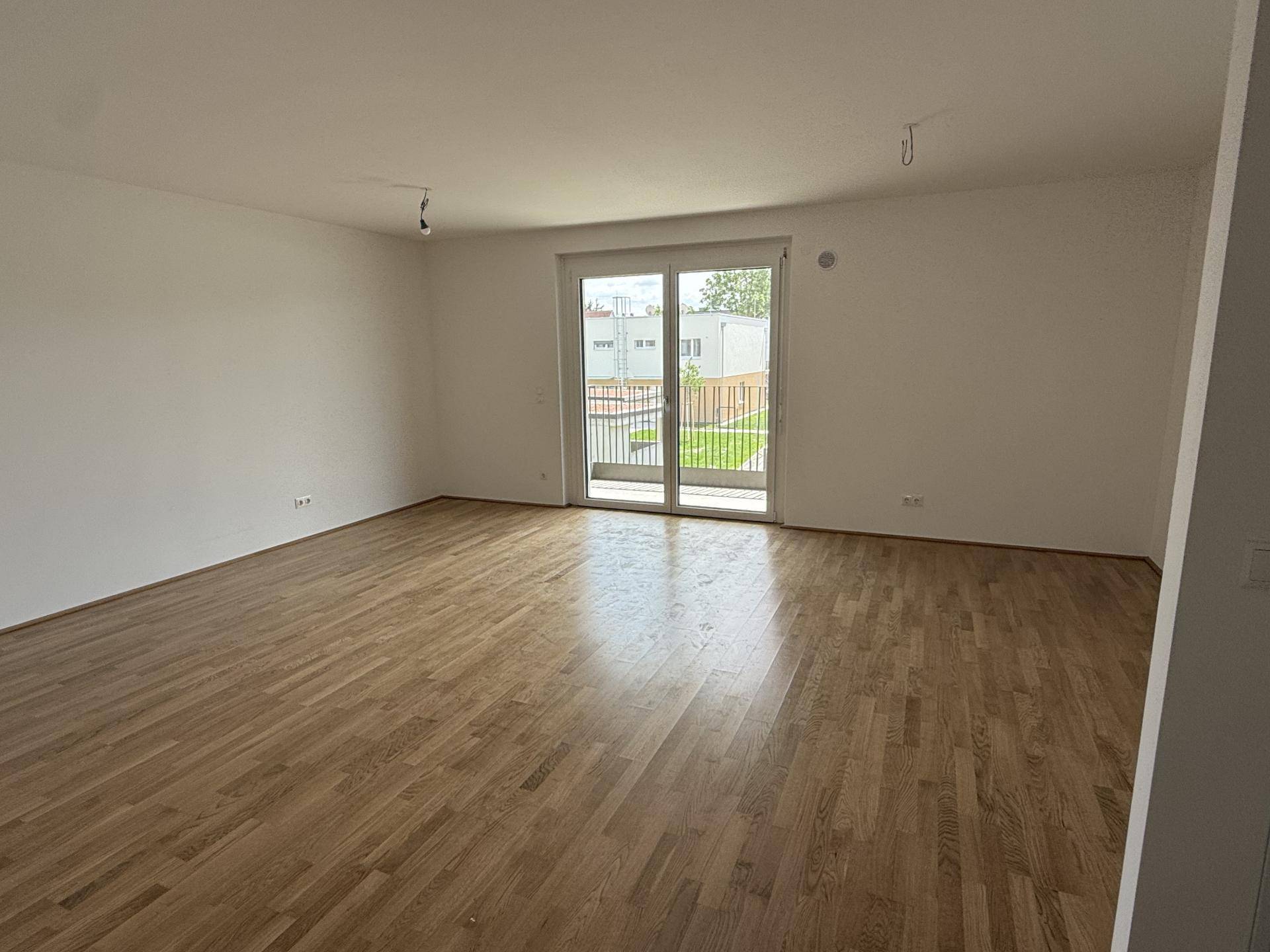 Geräumiges, helles Wohnzimmer mit Eichenparkett und Zugang zu einem Balkon.