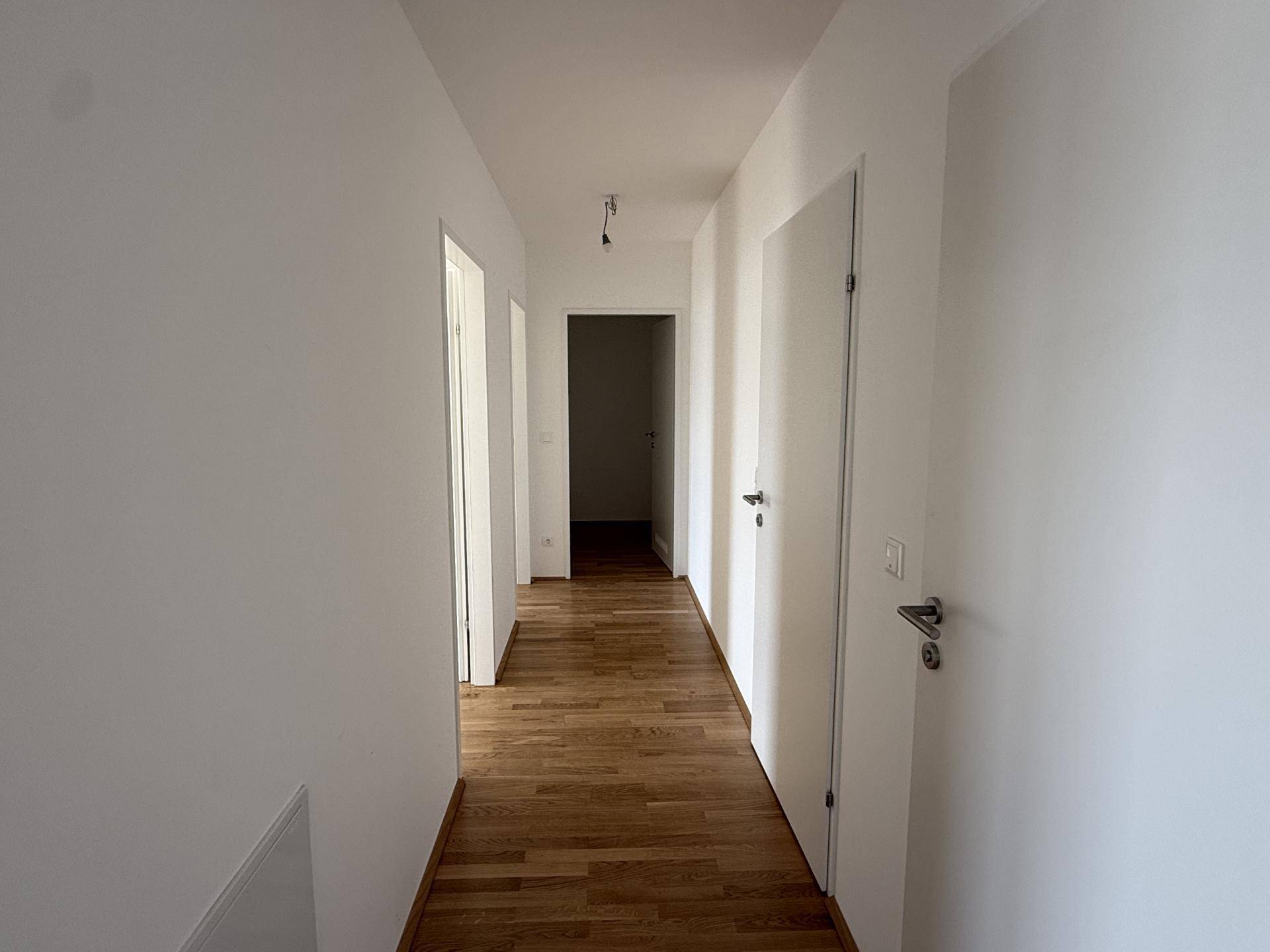 Langer, heller Flur mit Holzboden und weißen Wänden, der zu weiteren Räumen führt.