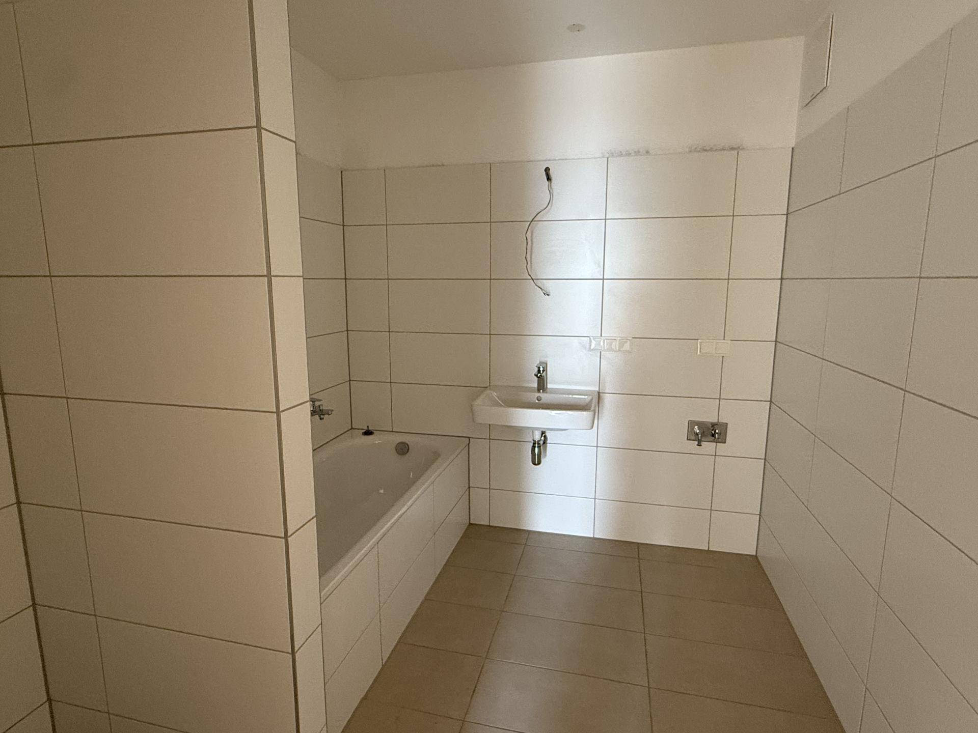 Unfertiges Badezimmer mit weißen Fliesen, Badewanne und Waschbecken.
