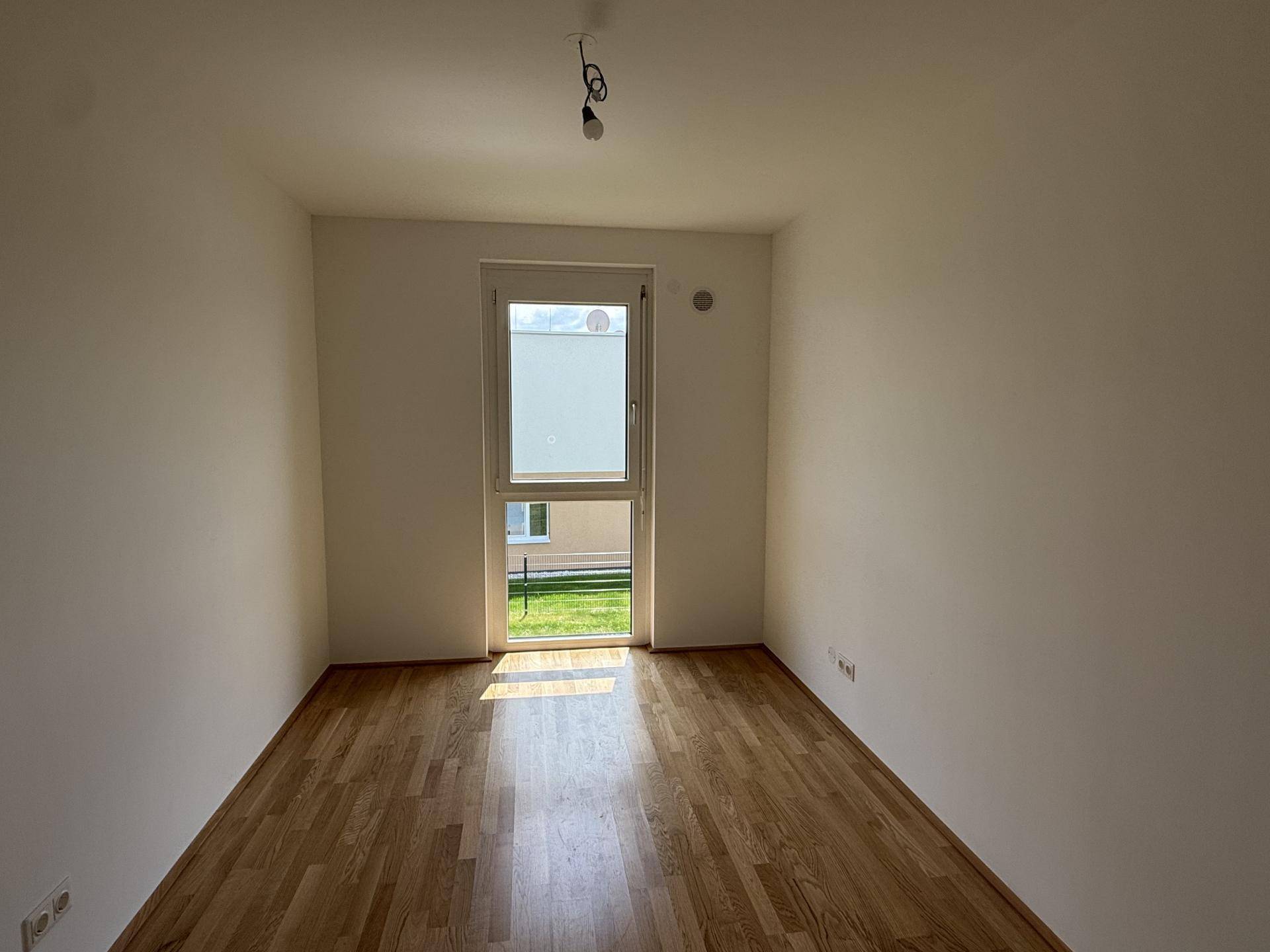 Helles Zimmer mit Holzboden und großem Fenster, das viel Tageslicht hereinlässt.