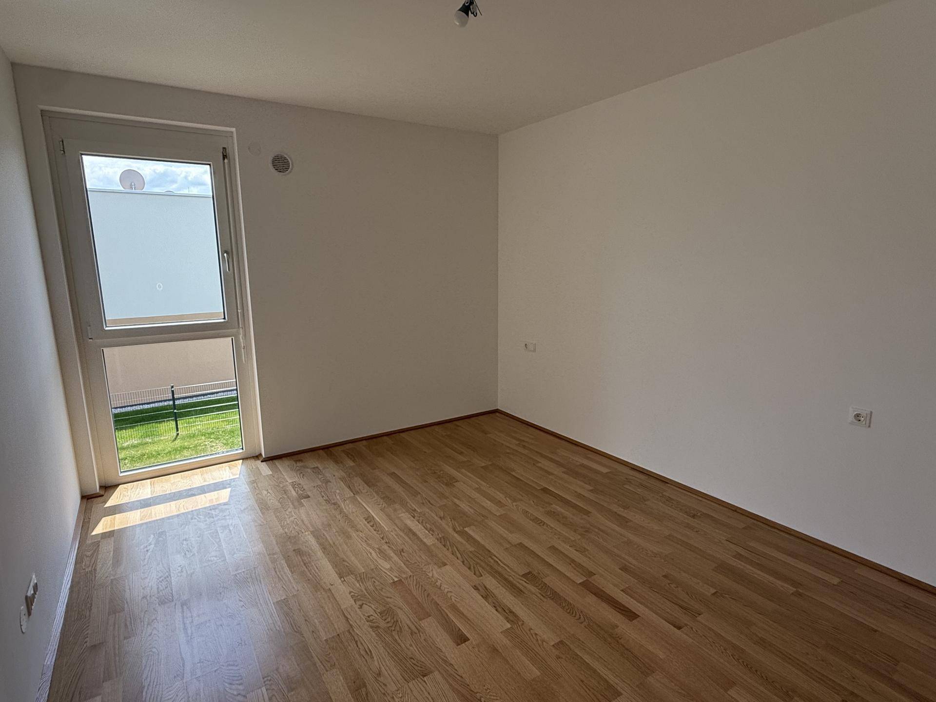 Sonniger Raum mit Holzboden und Fenster, das einen Blick ins Grüne bietet.