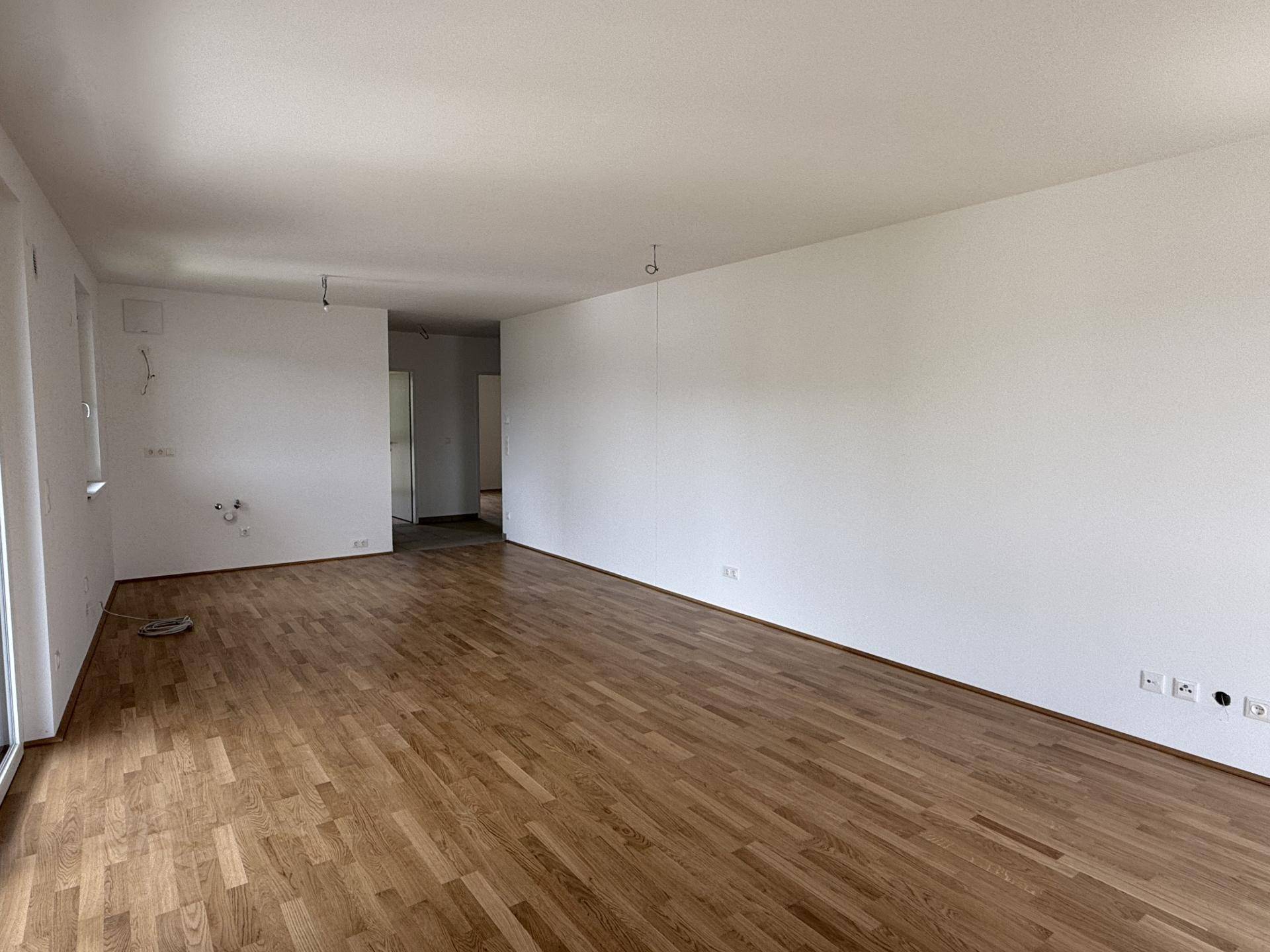 Geräumiges Wohnzimmer mit hellem Holzparkett und weißen Wänden, bereit für die Einrichtung.