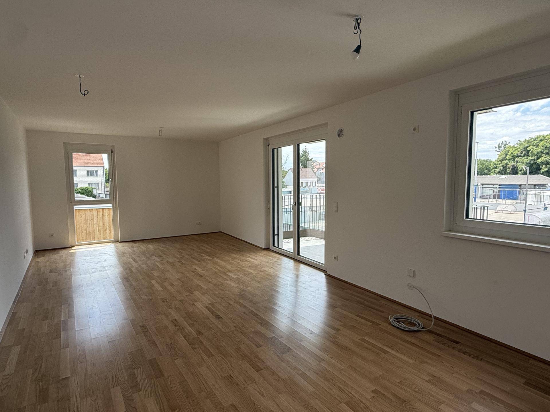 Lichtdurchflutetes Wohnzimmer mit Holzboden und Zugang zu einem Balkon, bietet viel Tageslicht.
