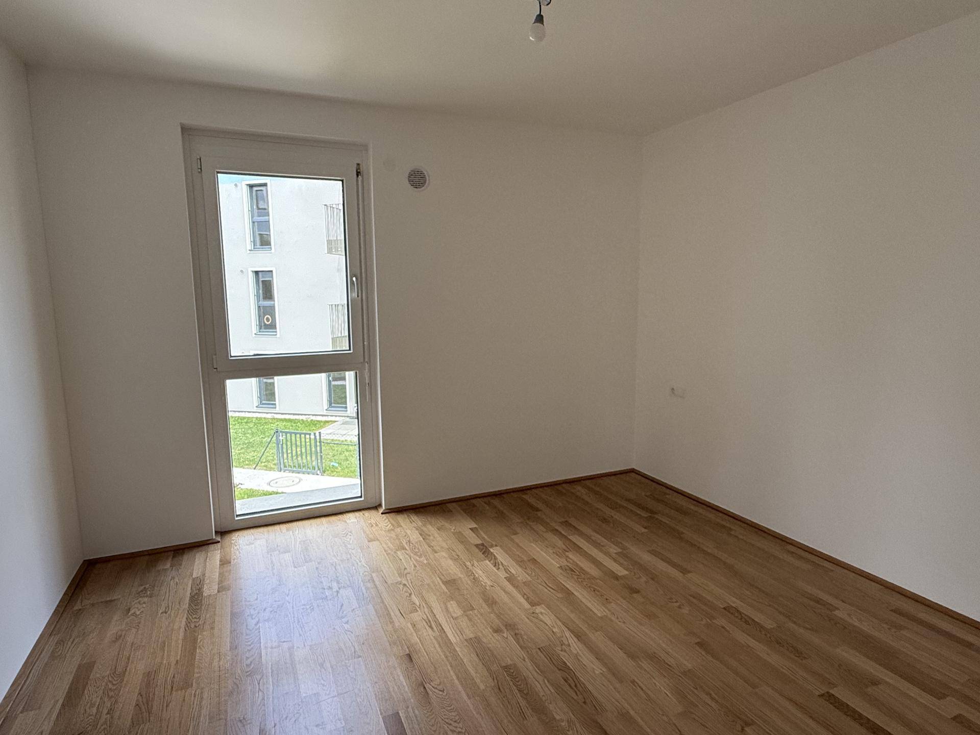 Helles Schlafzimmer mit Holzboden und großem Fenster, das einen Blick ins Grüne bietet.