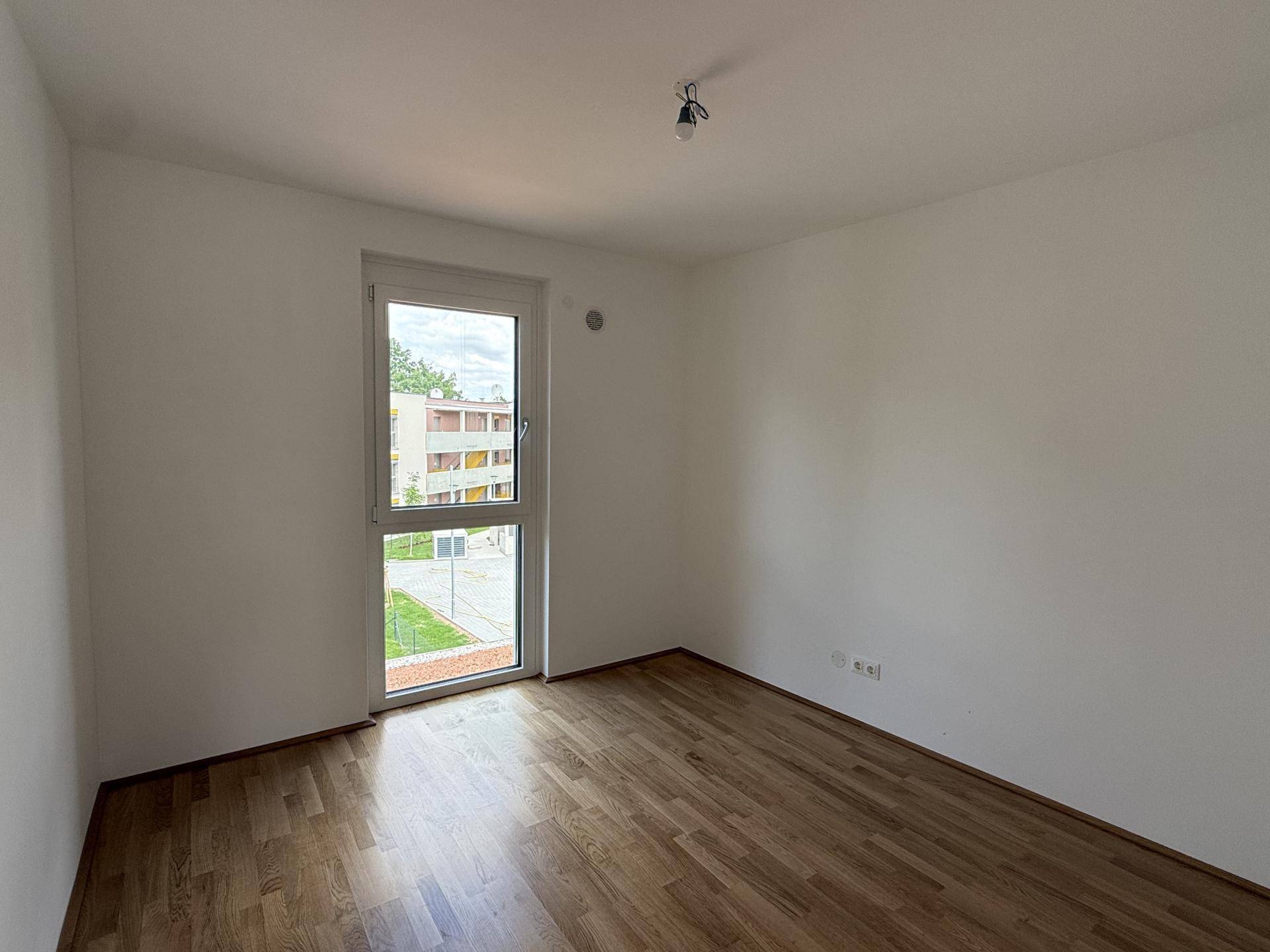 Helles Schlafzimmer mit Parkettboden und einem großen Fenster, das viel Tageslicht hereinlässt.