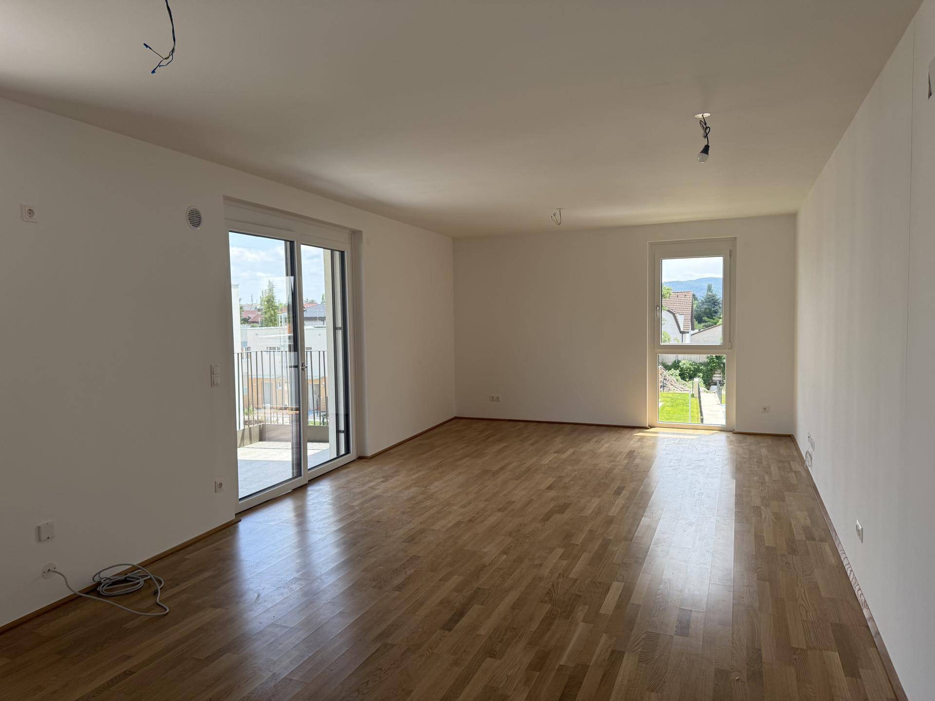 Geräumiges Wohnzimmer mit hellem Parkettboden, großen Fenstern und direktem Balkonzugang.
