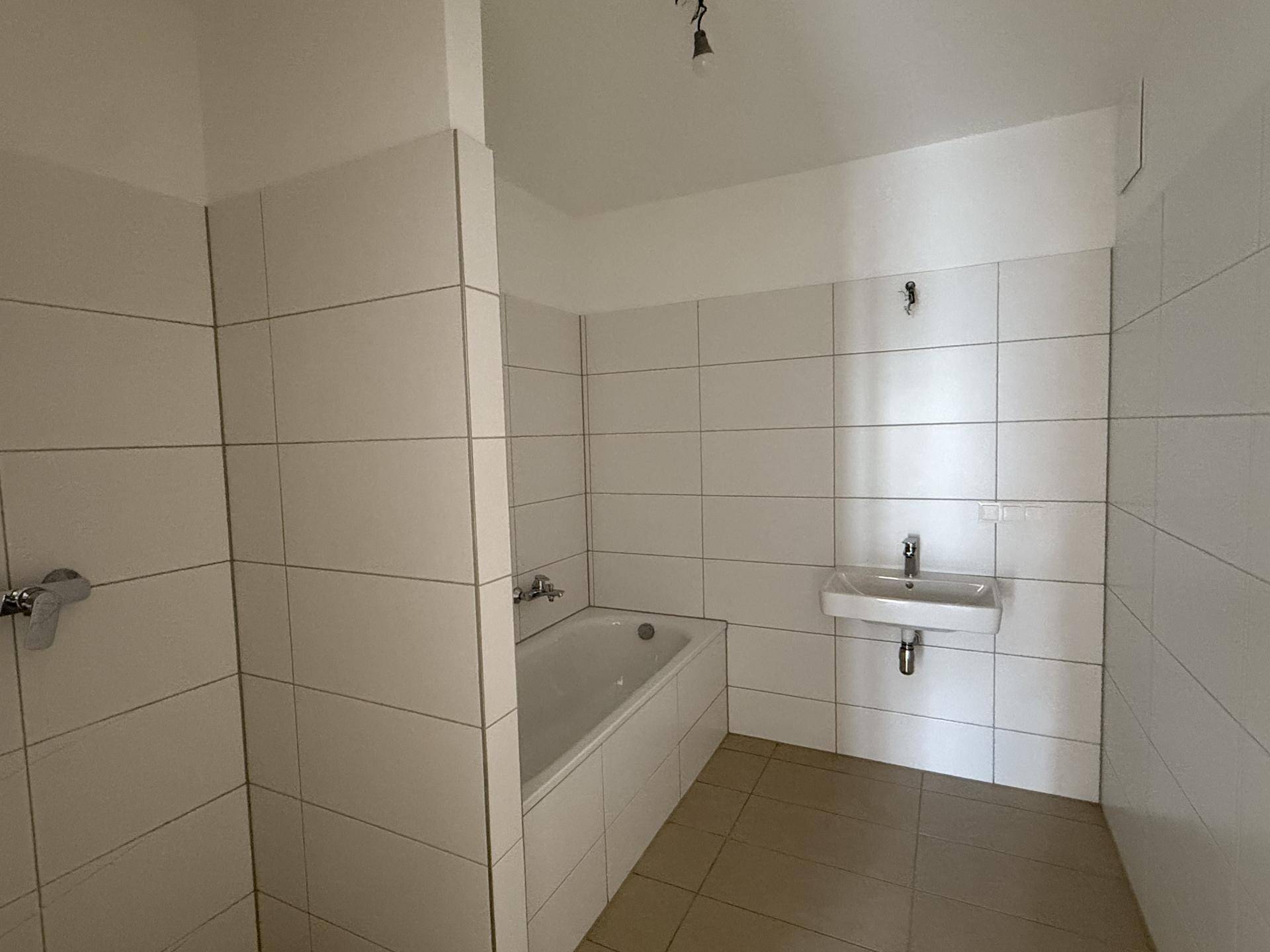 Modernes Badezimmer mit weißen Fliesen, einer Badewanne und einem einzelnen Waschbecken.