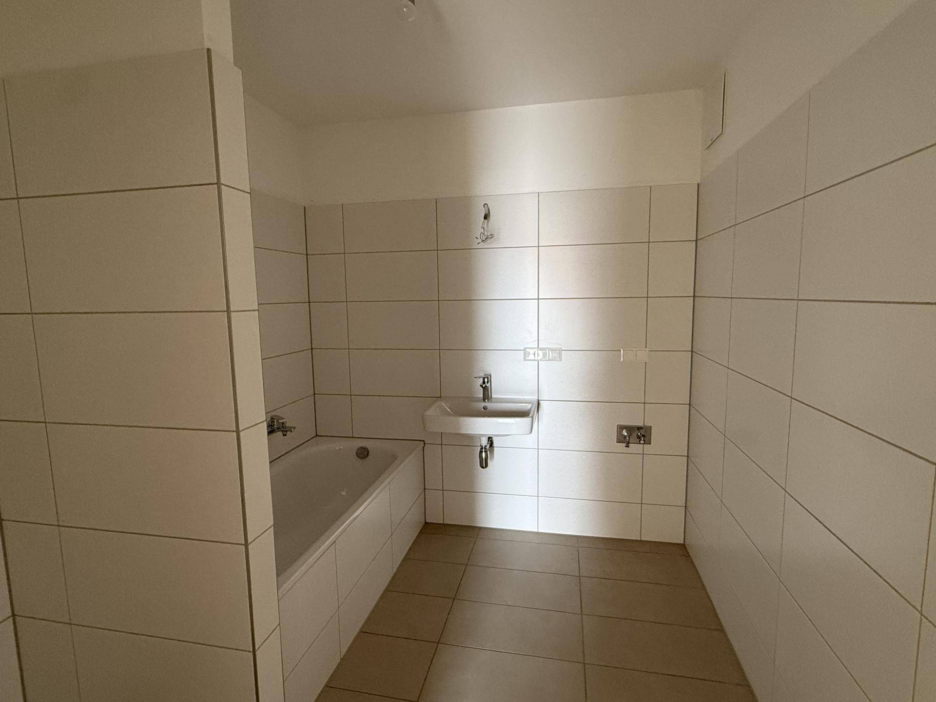 Badezimmer mit hellen Fliesen, einer Badewanne und einem einzelnen Waschbecken.