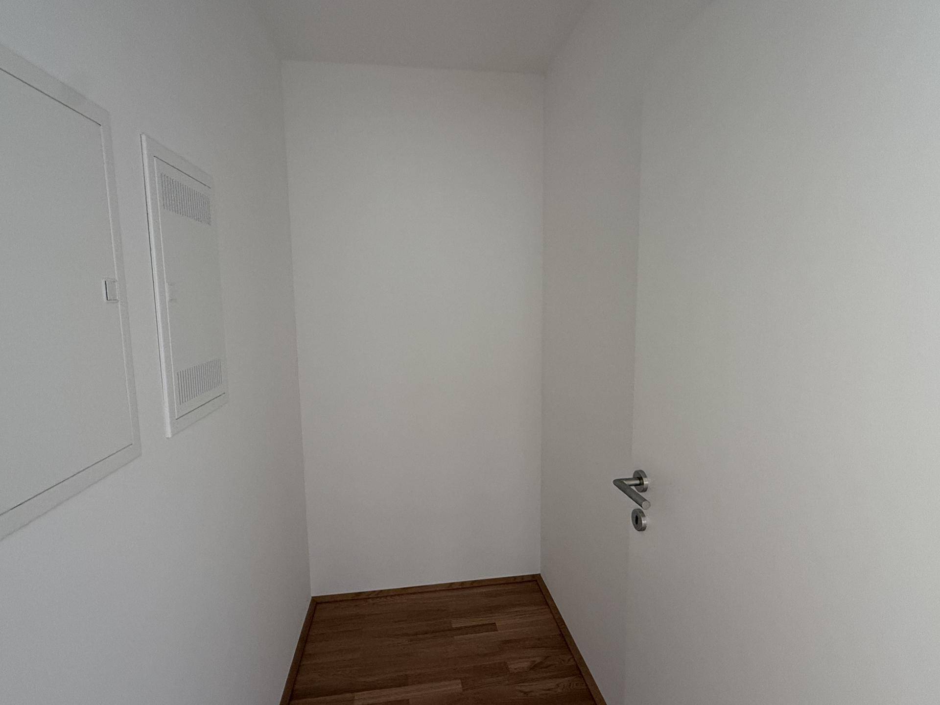Kleiner Abstellraum oder Technikraum mit weißen Wänden und Holzboden.