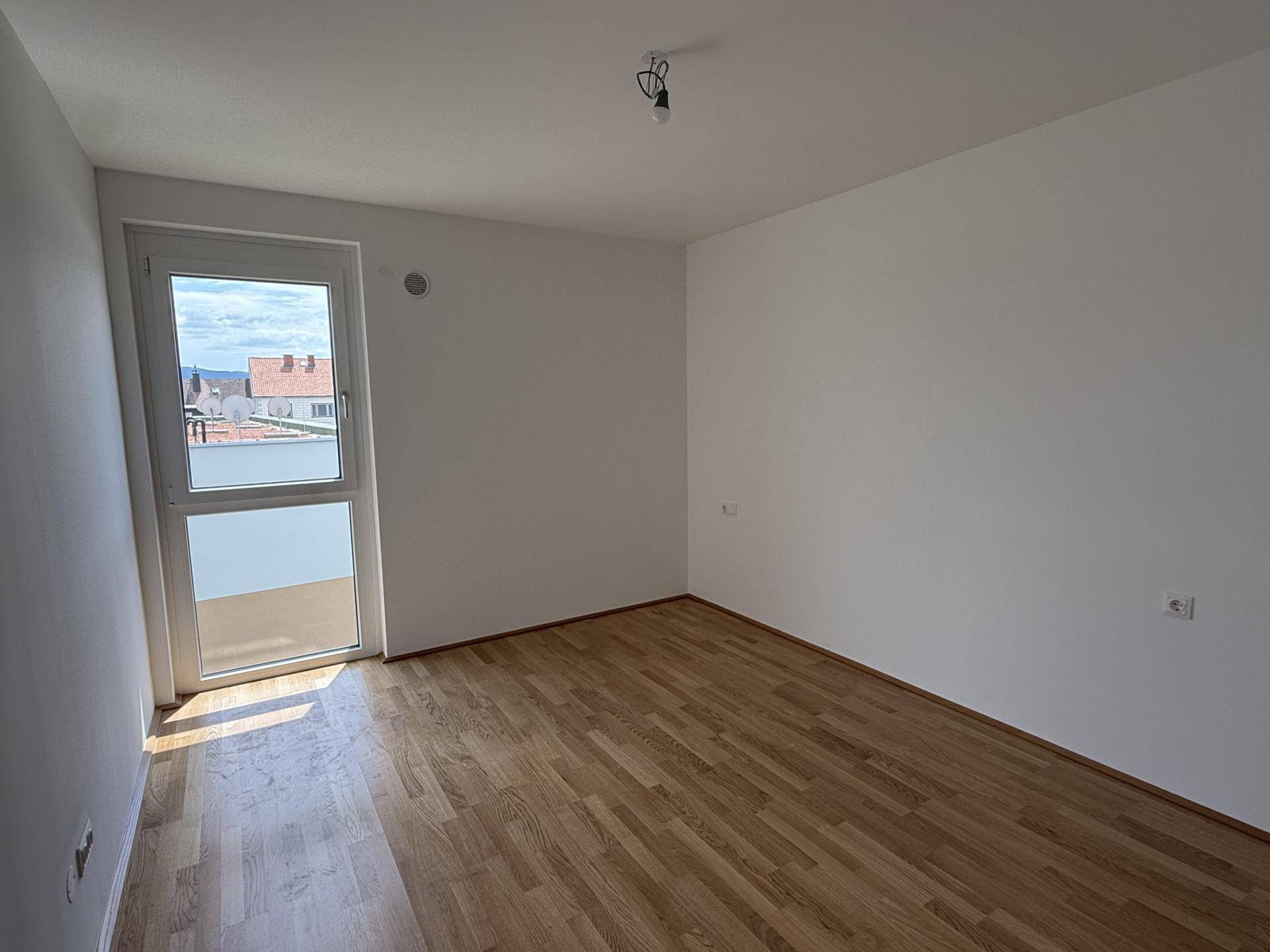 Freundliches Zimmer mit Parkettboden und Fenster, das einen Blick auf die Umgebung bietet.