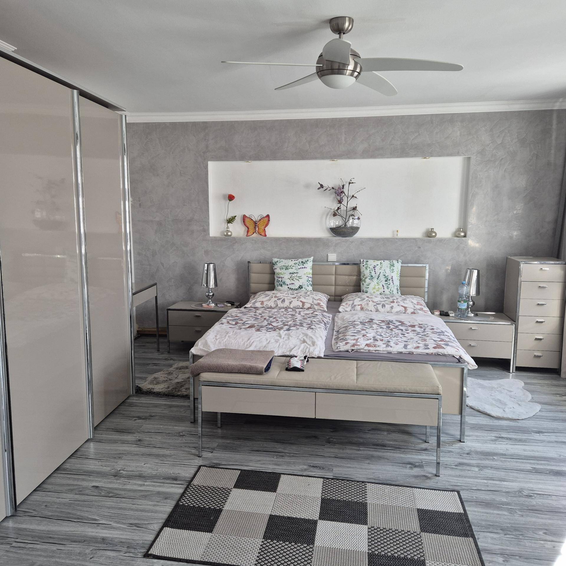 Modernes Schlafzimmer mit Doppelbett, großem Kleiderschrank und Deckenventilator.
