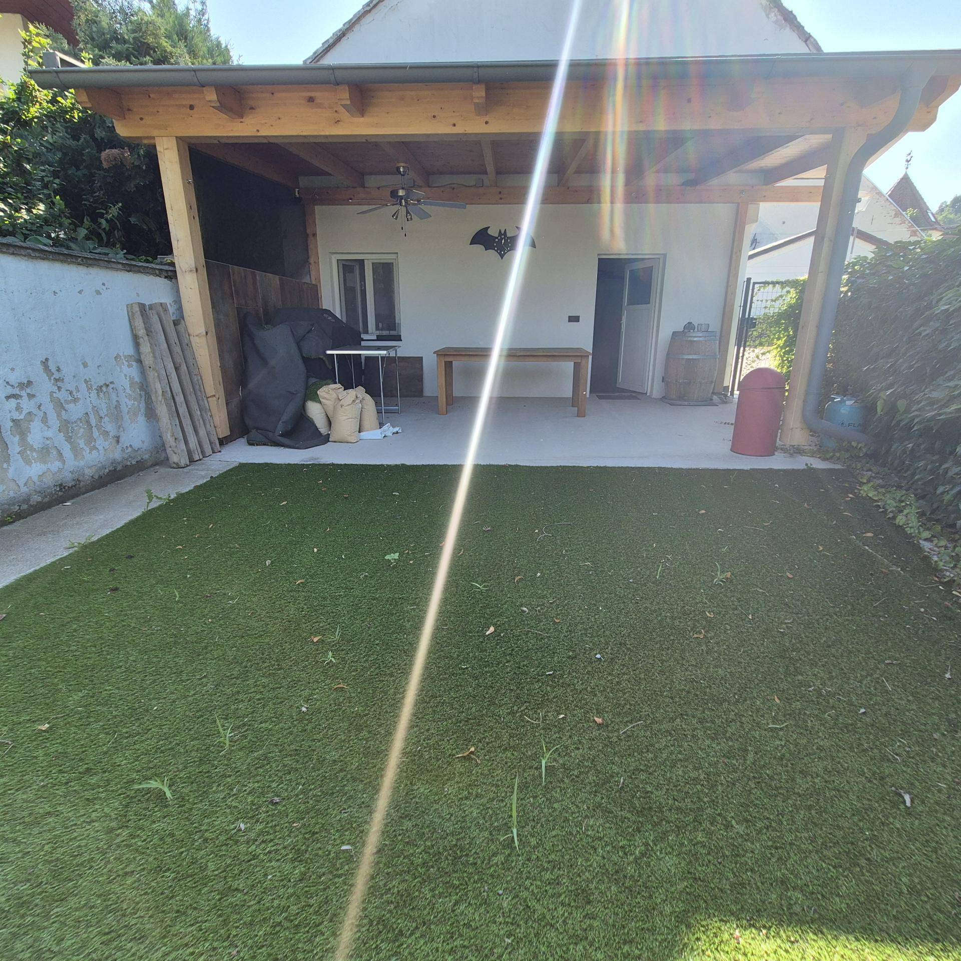 Gartenbereich mit Kunstrasen und einer überdachten Terrasse, ideal für Entspannung im Freien.