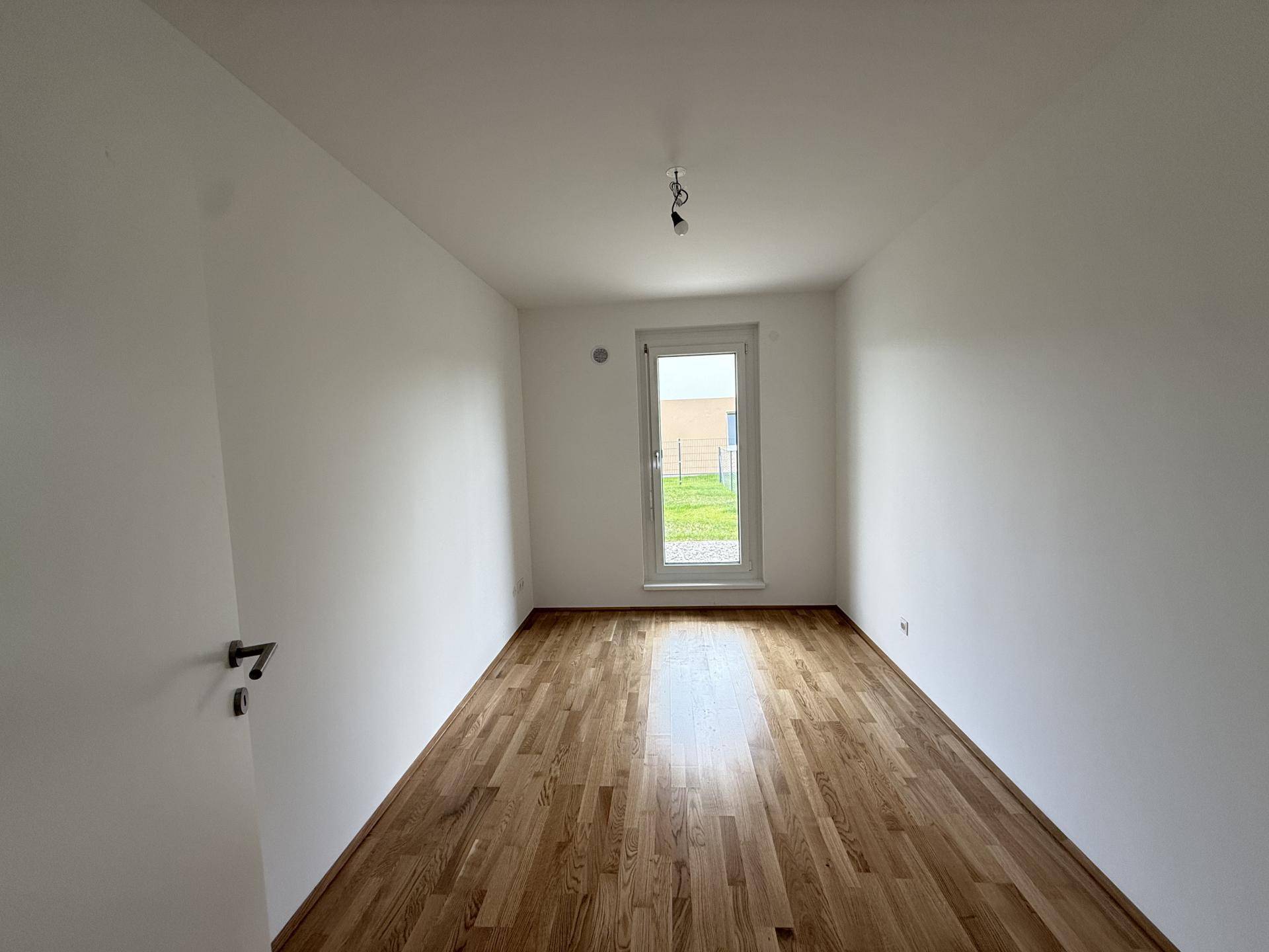 Schlafzimmer mit Holzboden, weißen Wänden und Fenster mit Blick ins Grüne.