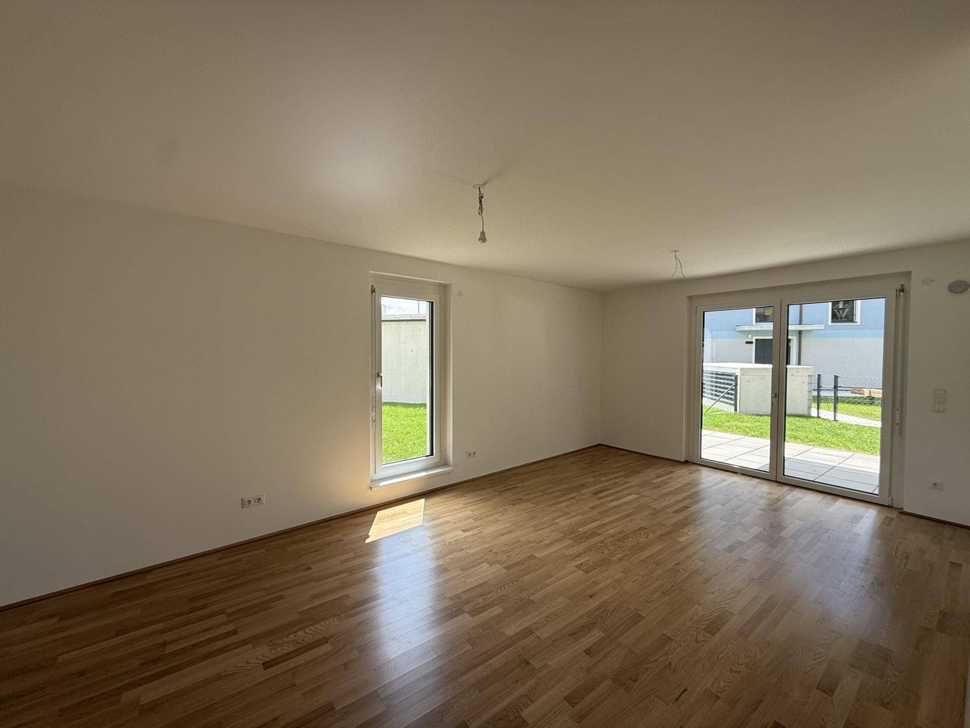 Helles Wohnzimmer mit Holzboden, weißen Wänden und Zugang zum Garten.