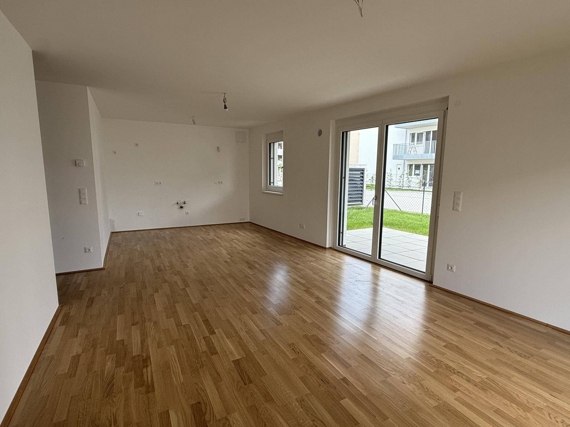 Geräumiges Wohnzimmer mit Holzboden und großen Fenstern, die viel Tageslicht hereinlassen.