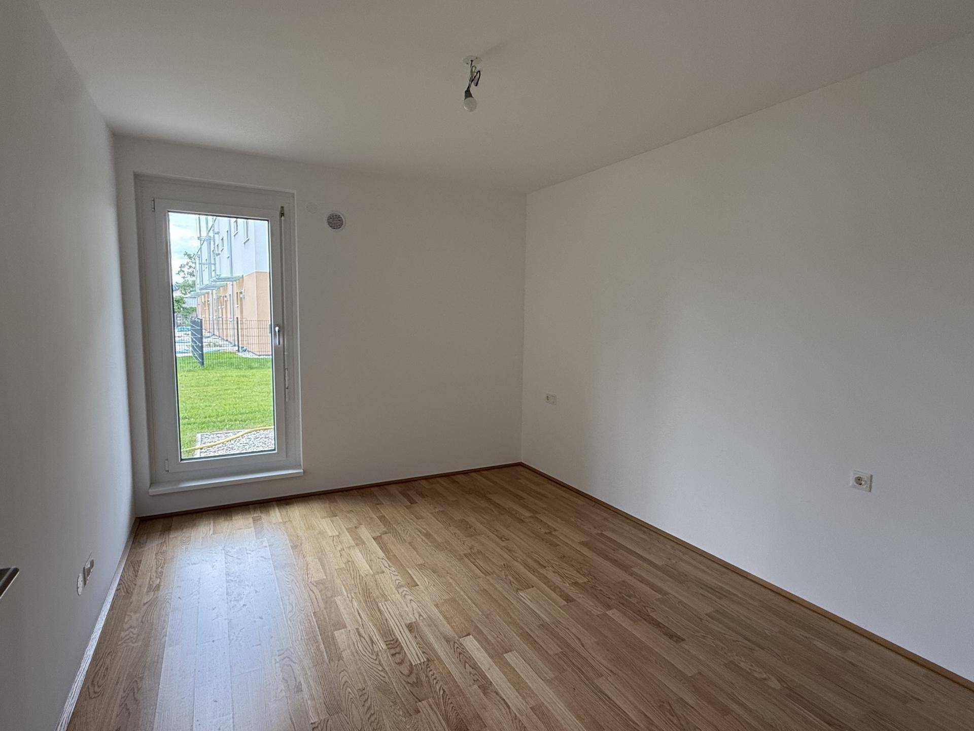 Helles Schlafzimmer mit Holzboden und großem Fenster, das den Raum gut belichtet.