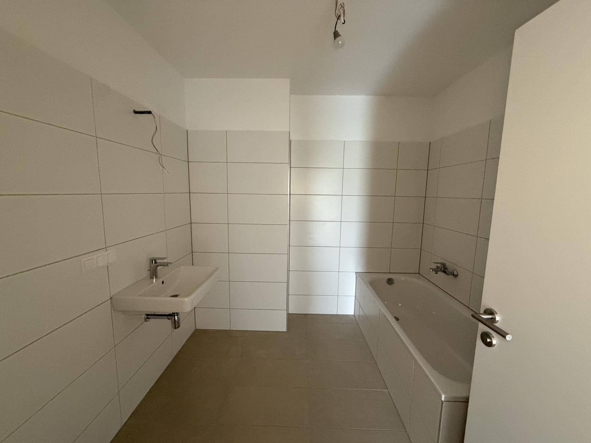 Modernes Badezimmer mit weißen Fliesen, Waschbecken und eingebauter Badewanne.