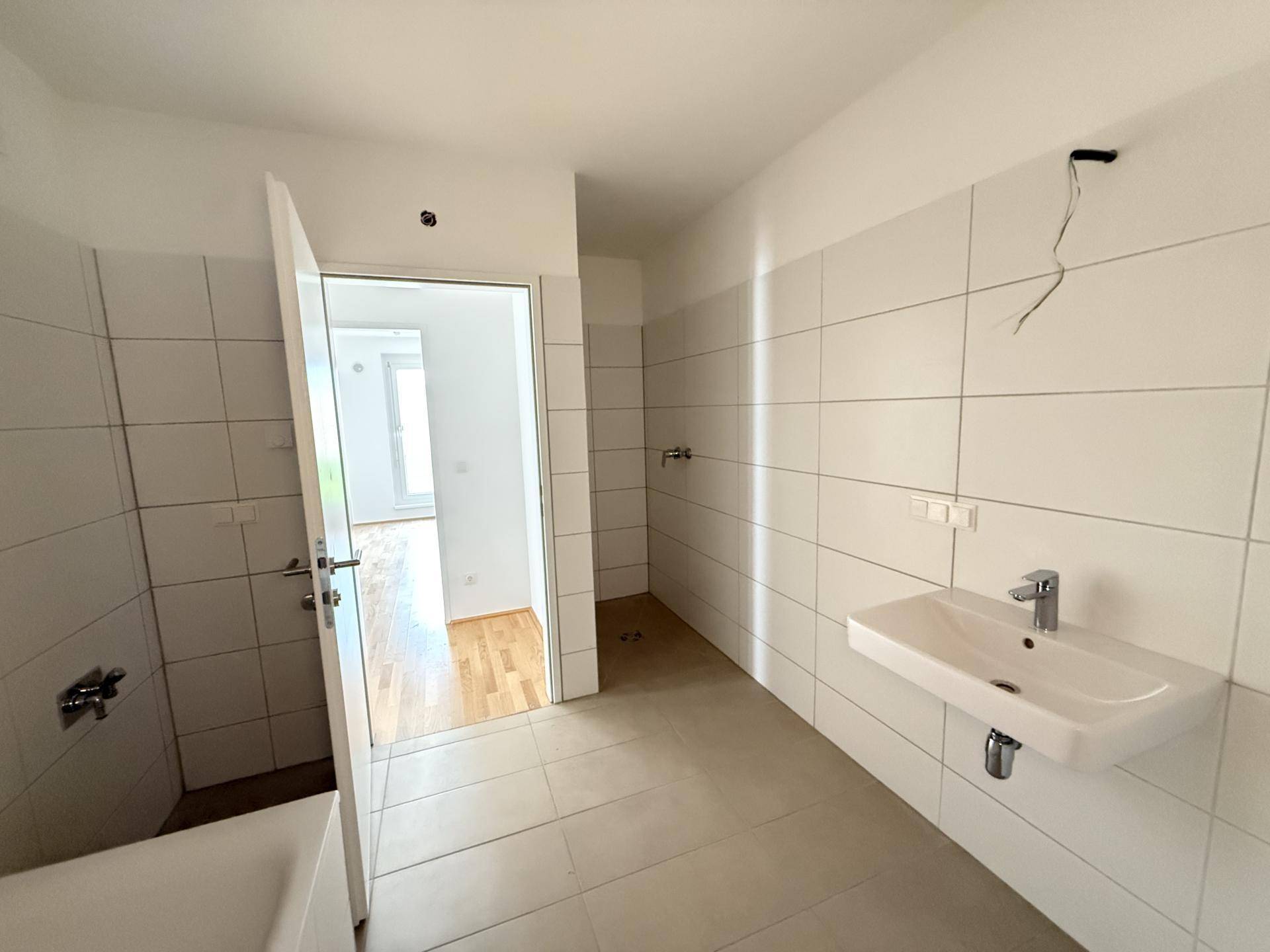 Badezimmer mit weißen Wandfliesen, Waschbecken und Badewanne, bereit für die Fertigstellung.