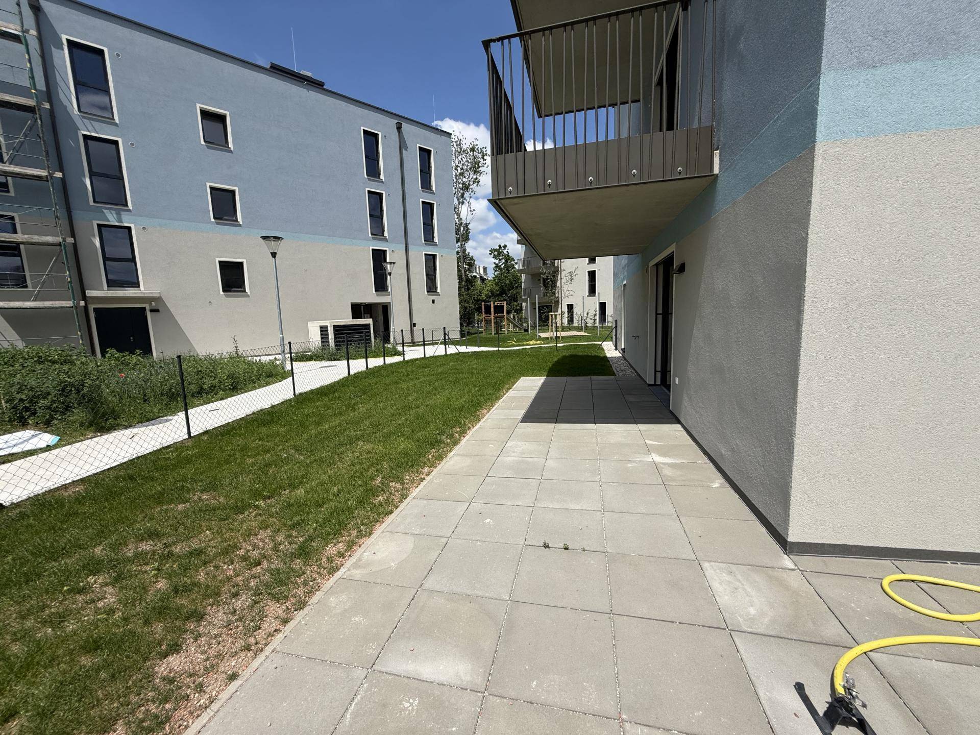 Geräumige gepflasterte Terrasse neben dem Gebäude mit Zugang zur Rasenfläche und Balkon darüber.