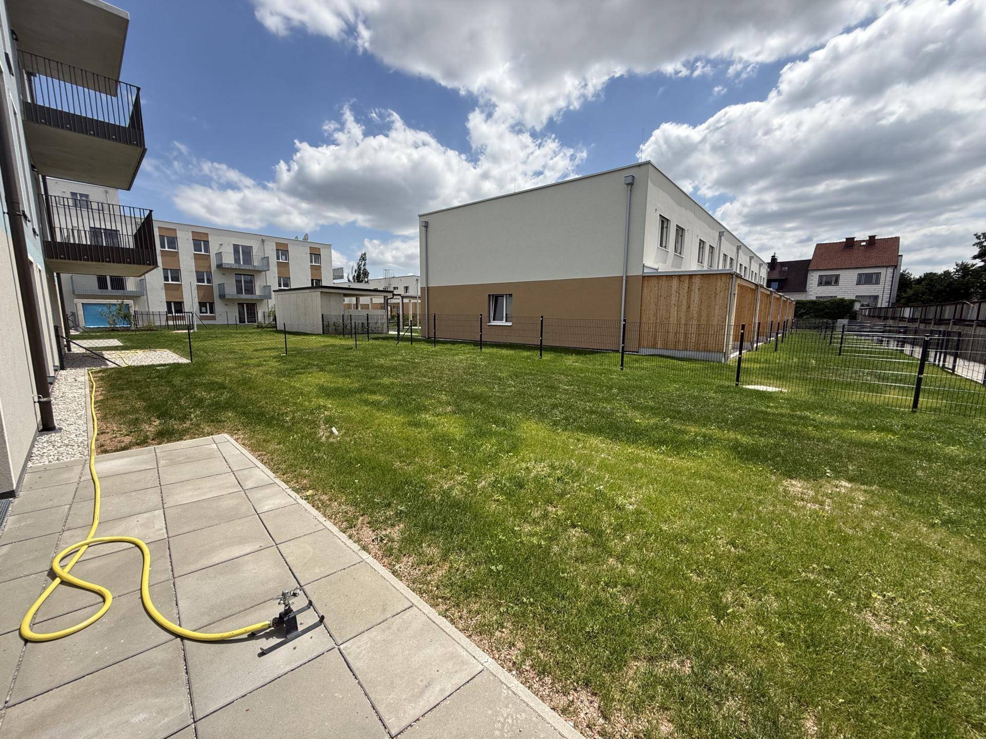 Gepflasterte Terrasse mit Rasenfläche und Blick auf weitere Wohngebäude in der Umgebung.