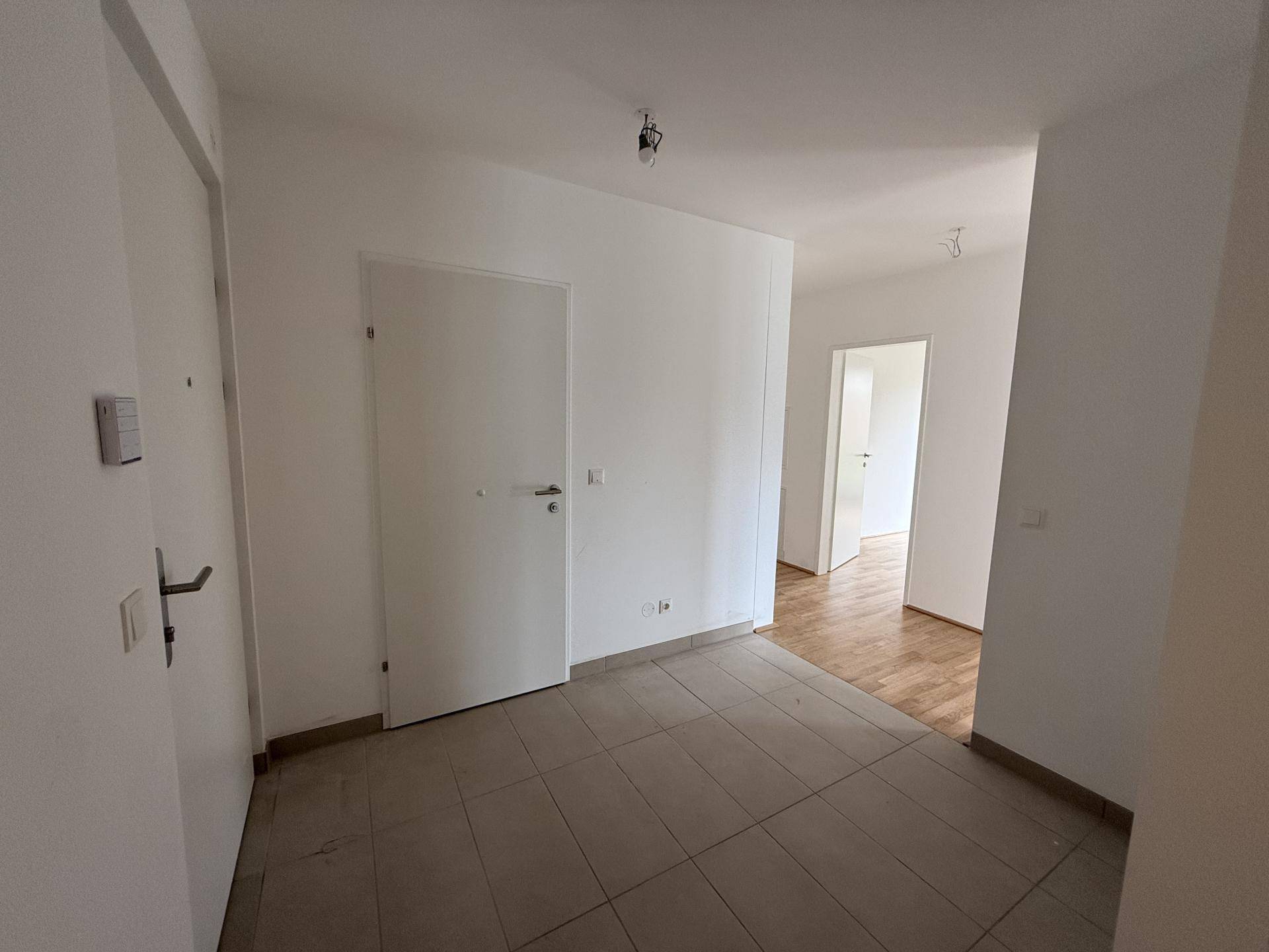 Heller Eingangsbereich mit Fliesenboden und Übergang zu Räumen mit Holzparkett.