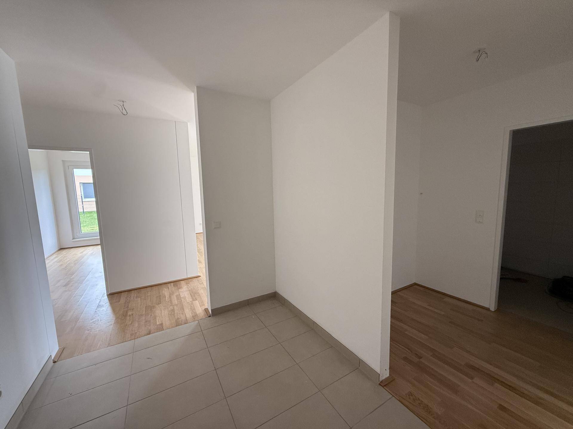 Geräumiger Flur mit hellen Fliesen und Blick in angrenzende Zimmer mit Holzfußboden.