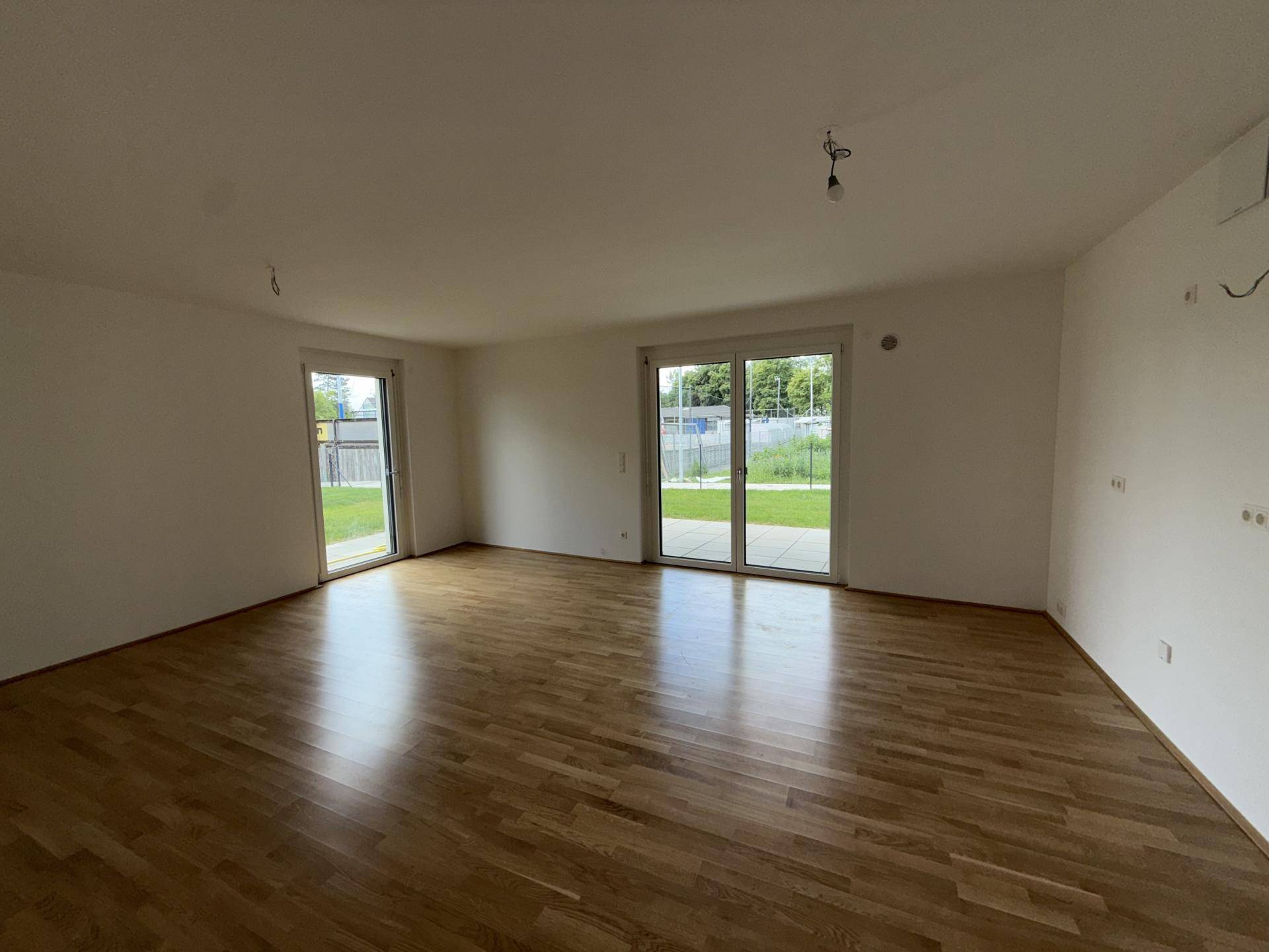 Großes, helles Wohnzimmer mit Holzparkett und zwei Terrassentüren zum Gartenbereich.