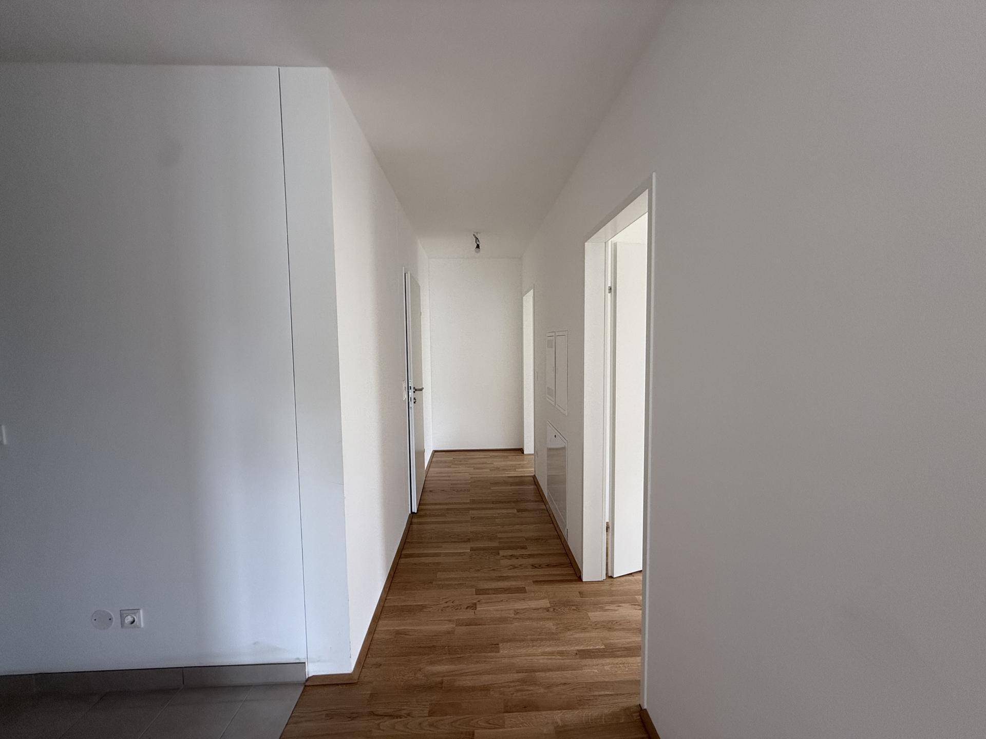 Langer, heller Flur mit glänzendem Holzparkett und weißen Wänden, der zu weiteren Räumen führt.