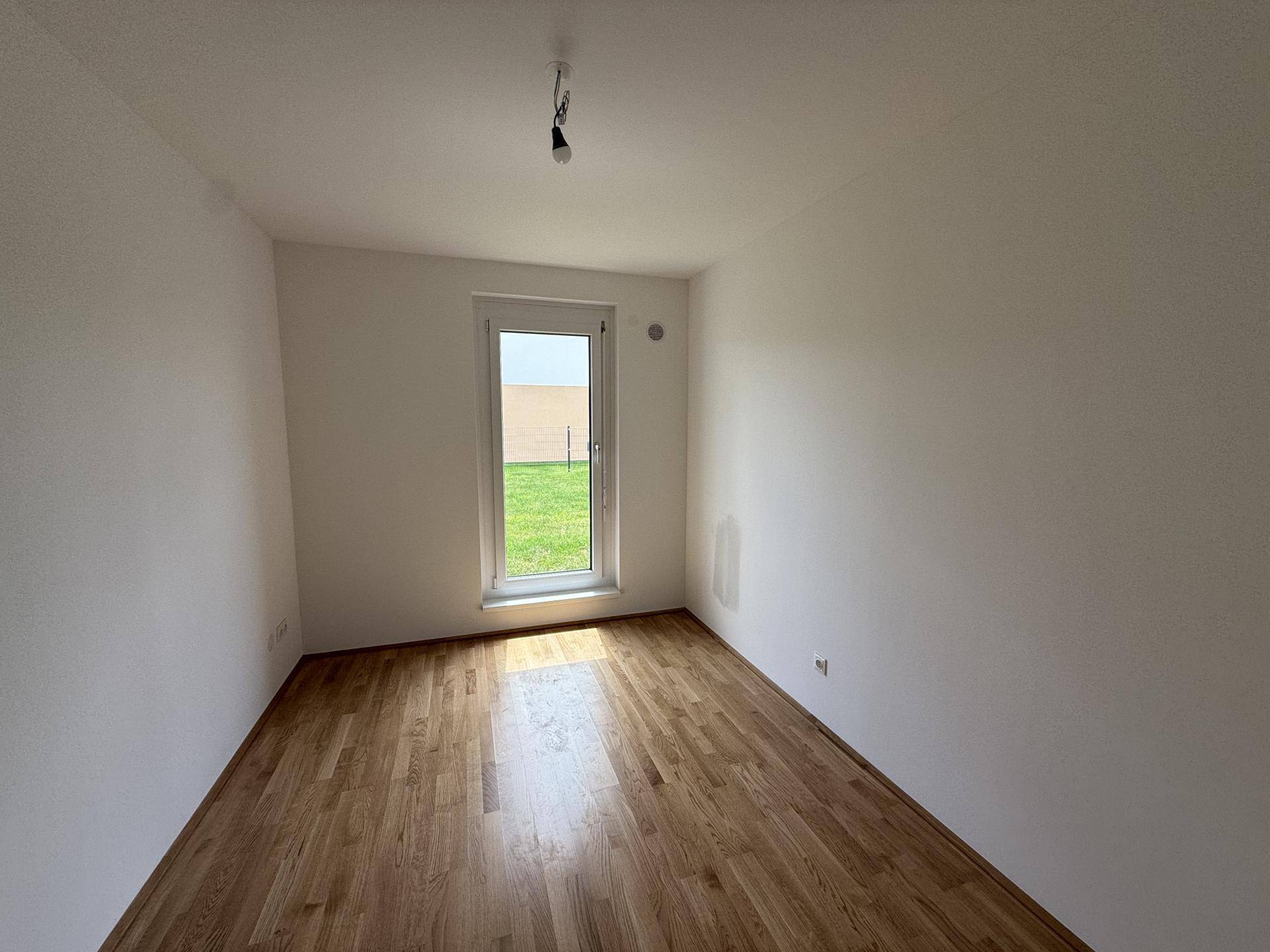 Freundliches Zimmer mit Holzfußboden und einer Fenstertür, die viel Tageslicht hereinlässt.