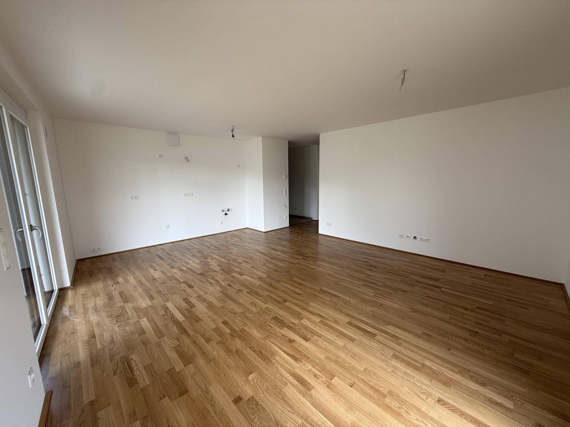 Geräumiges Wohnzimmer mit glänzendem Holzparkett und weißen Wänden, bereit zur individuellen Gestaltung.