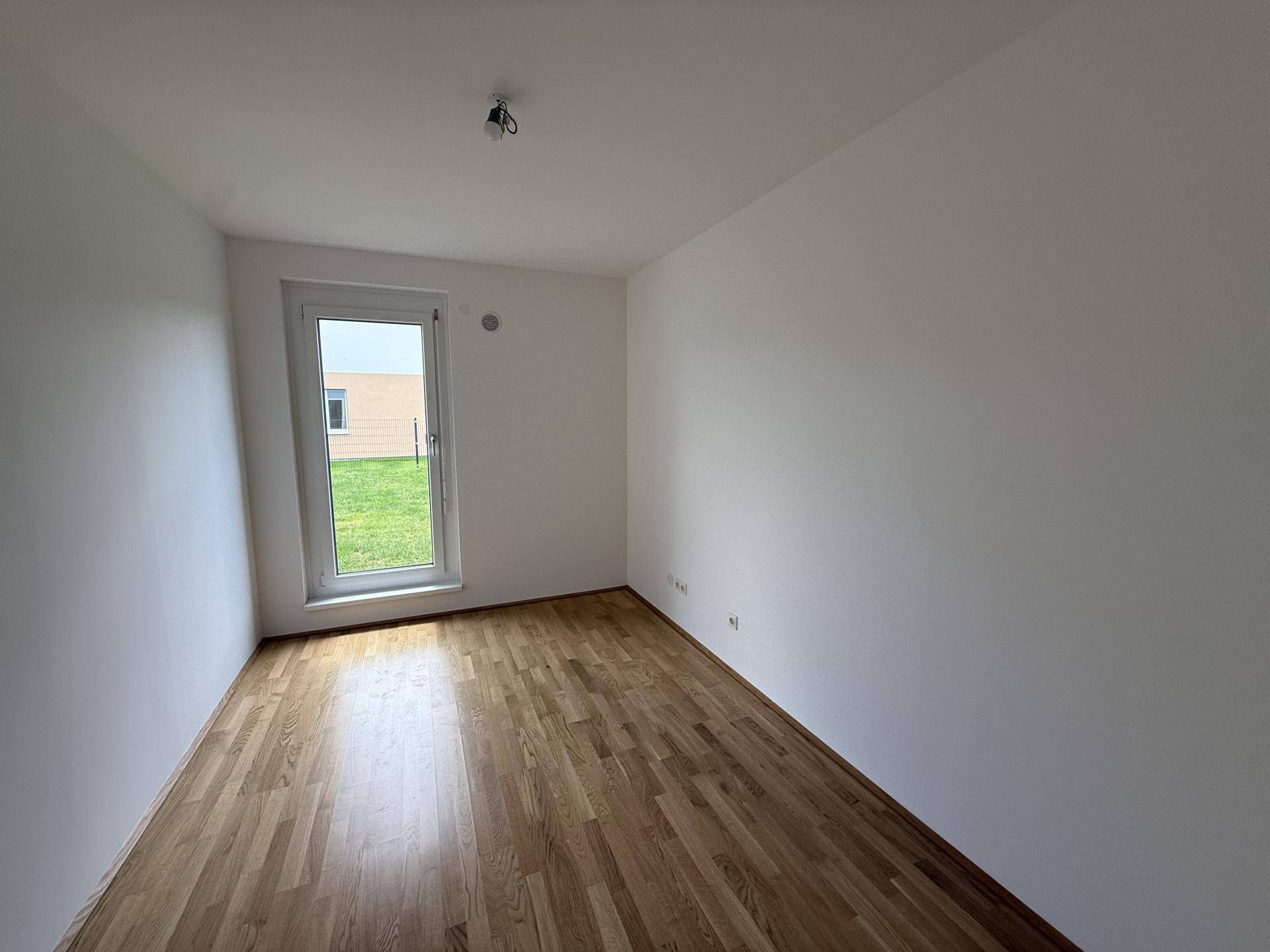 Helles Schlafzimmer mit Holzparkett und Zugang zu einer Grünfläche durch eine Fenstertür.