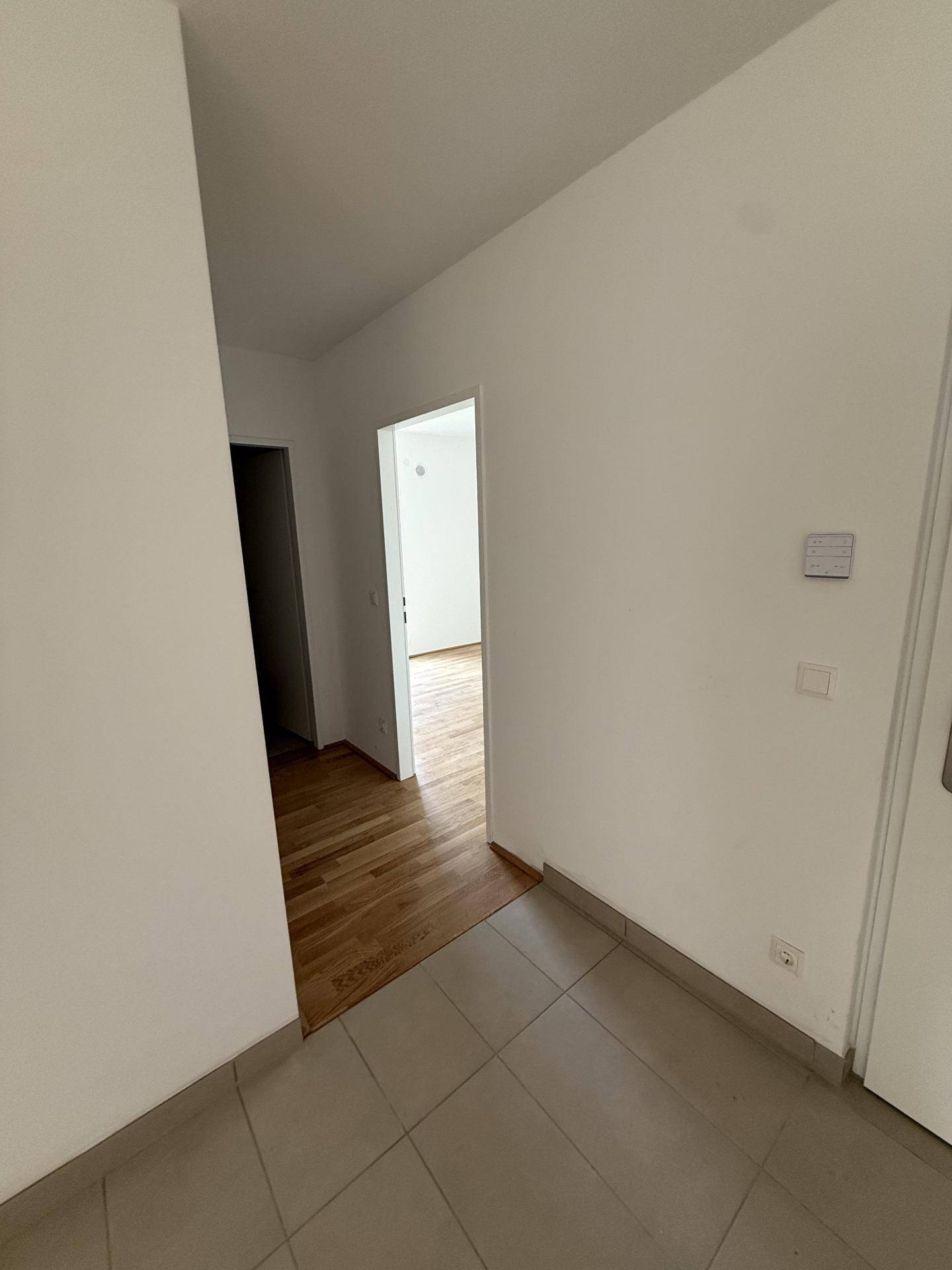 Heller Eingangsbereich mit Fliesenboden und Übergang zu Räumen mit Holzparkett.