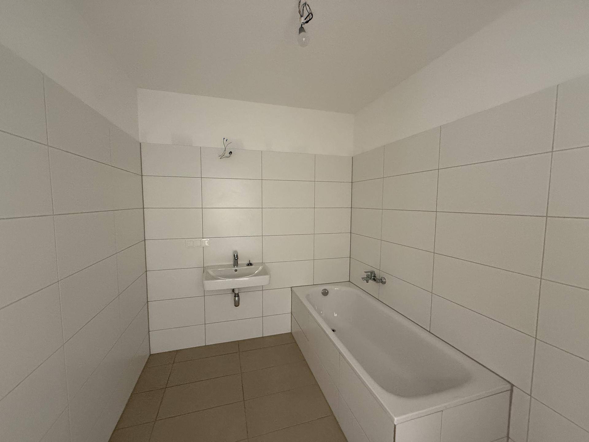 Modernes Badezimmer mit weißen Wandfliesen, beigem Boden und einer Badewanne mit Einzelwaschbecken.