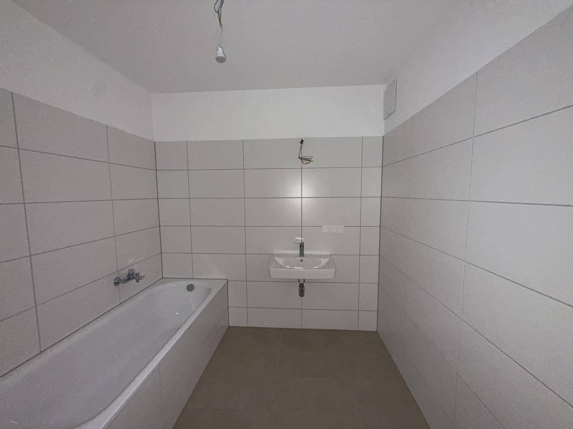 Modern gefliestes Badezimmer mit Badewanne und Waschbecken, bereit zur individuellen Gestaltung.