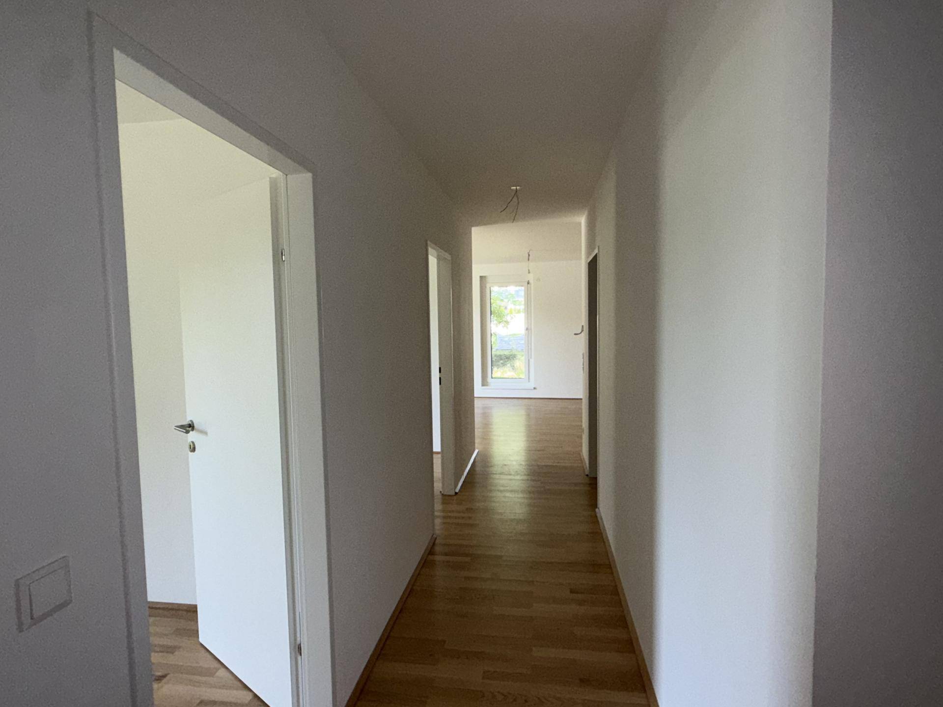 Langer, heller Flur mit Holzparkettboden und Blick in weitere Zimmer mit Tageslicht.