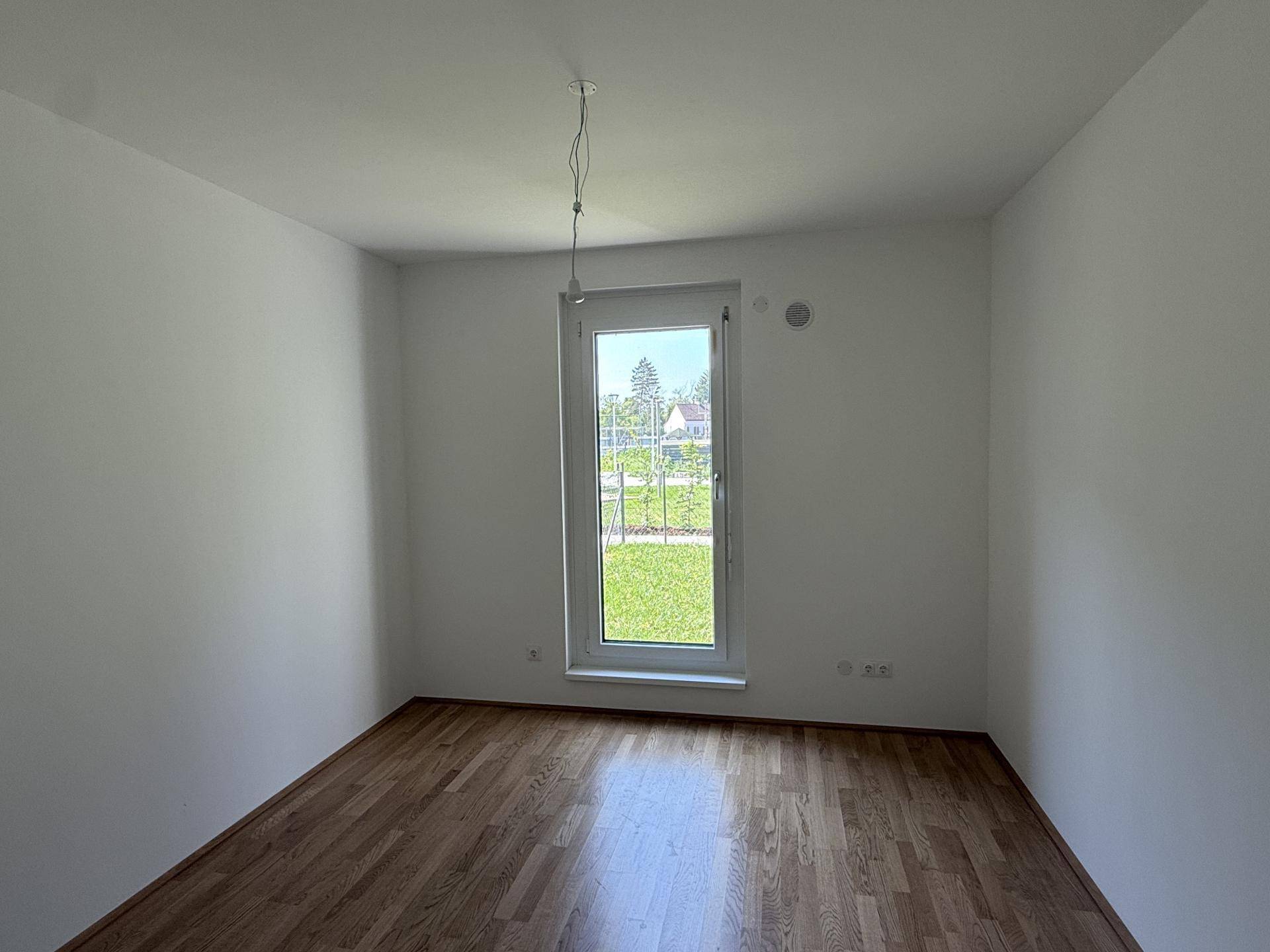 Helles Zimmer mit Parkettboden und großem Fenster, das einen schönen Blick ins Grüne bietet.