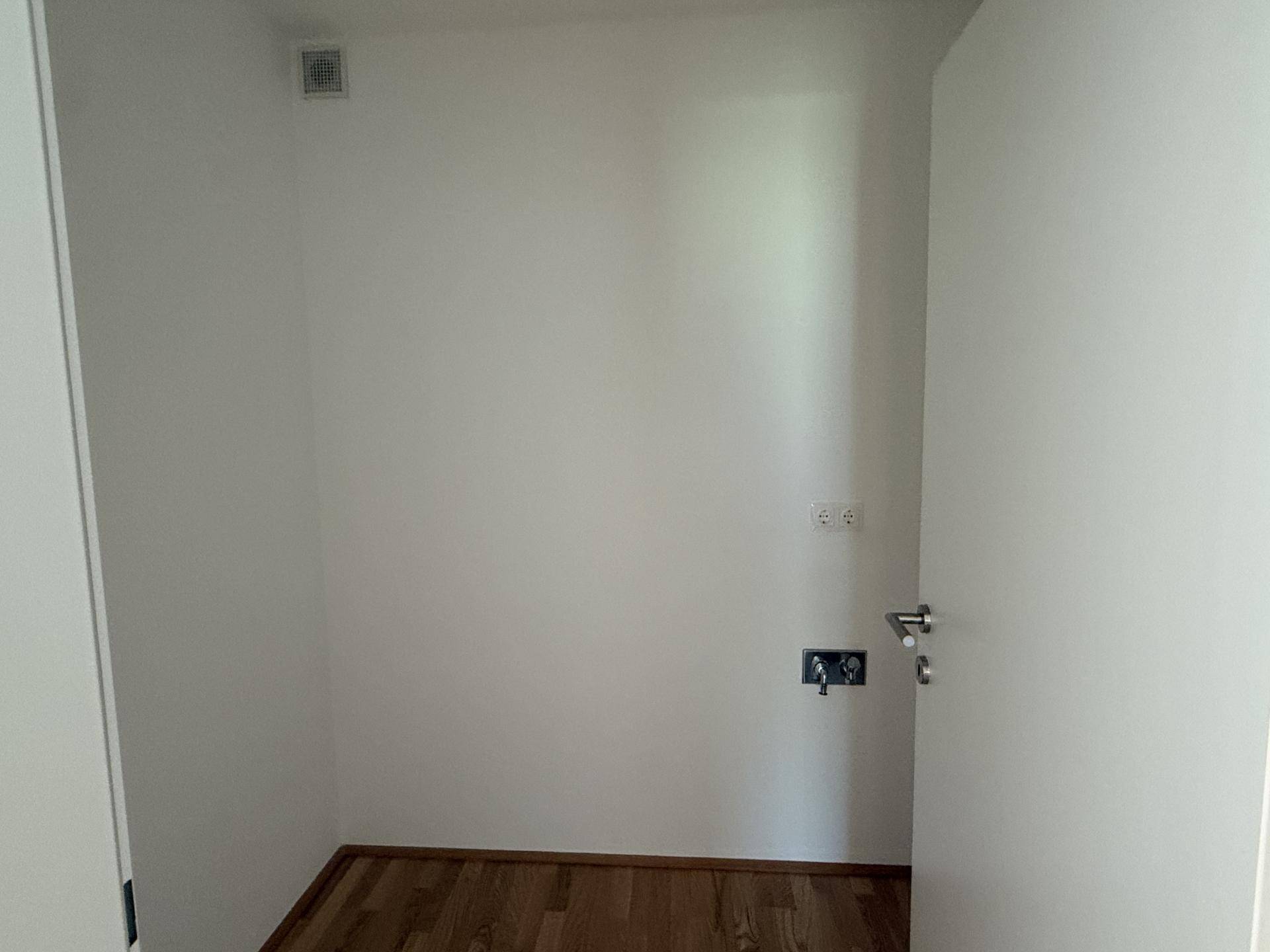 Kleiner Raum mit Anschlüssen für Waschmaschine oder eine mögliche Küchenzeile, unmöbliert.
